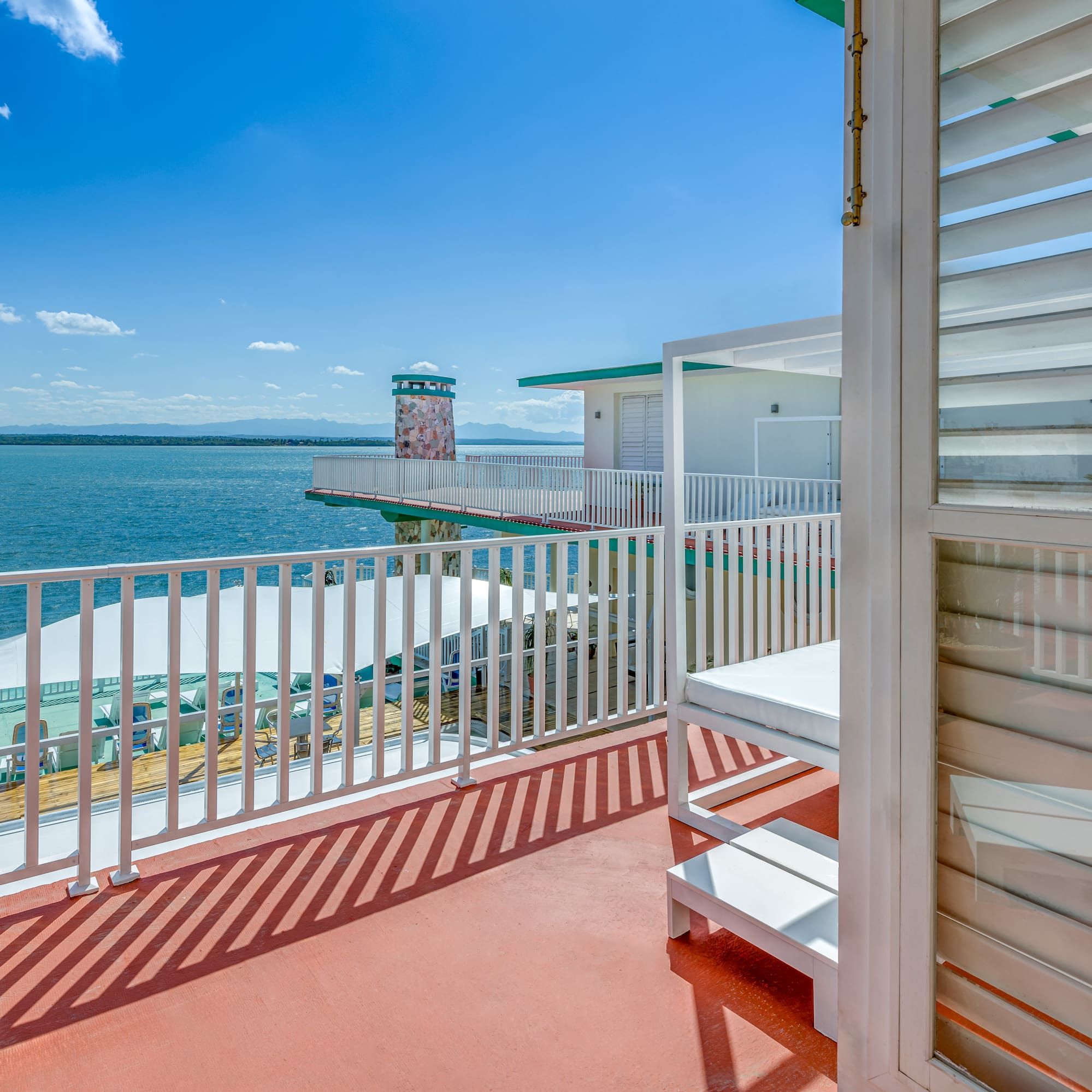 a deck with a white railing and a white building with a body of water in the background