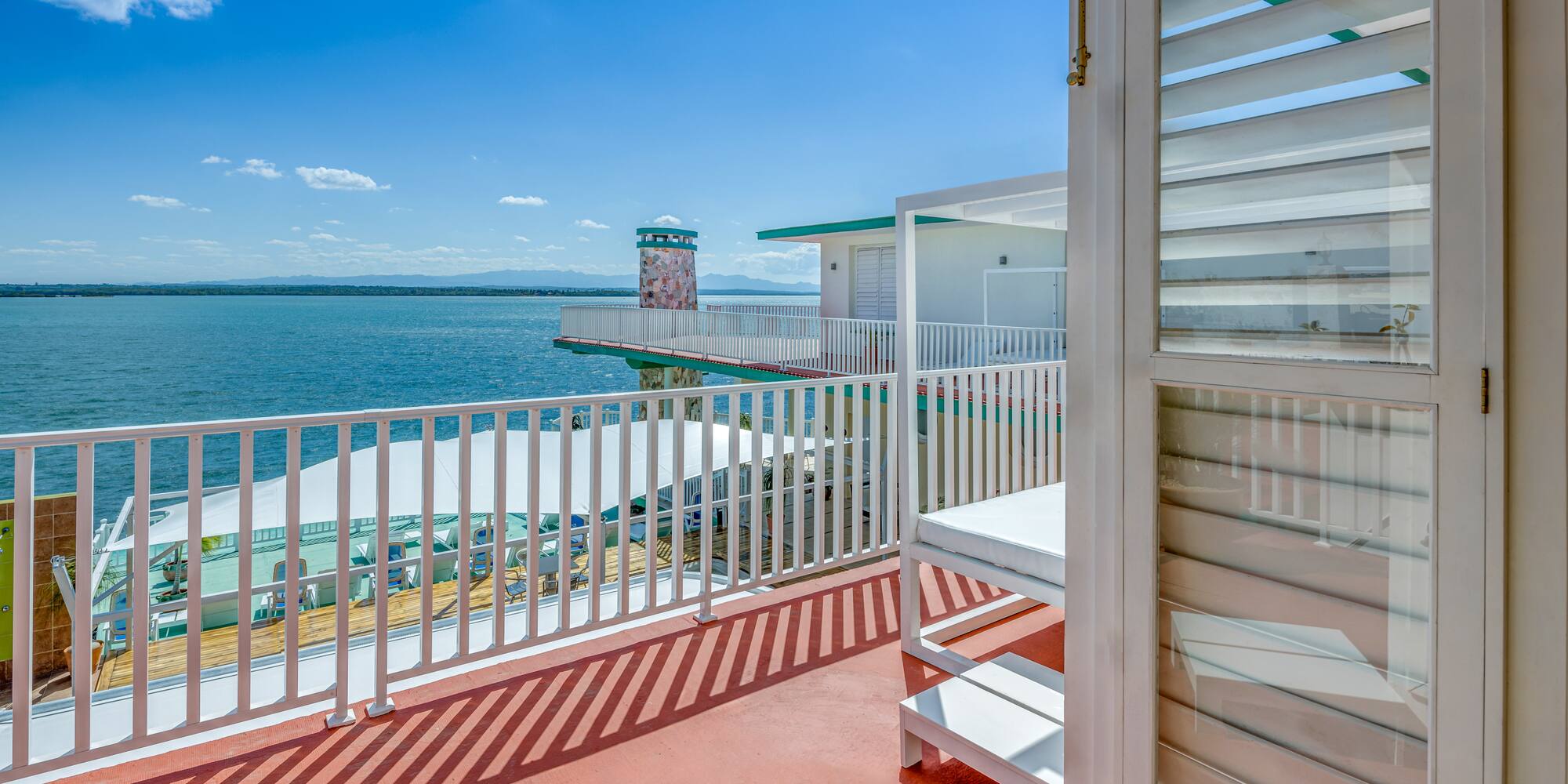 a deck with a white railing and a white building with a body of water in the background