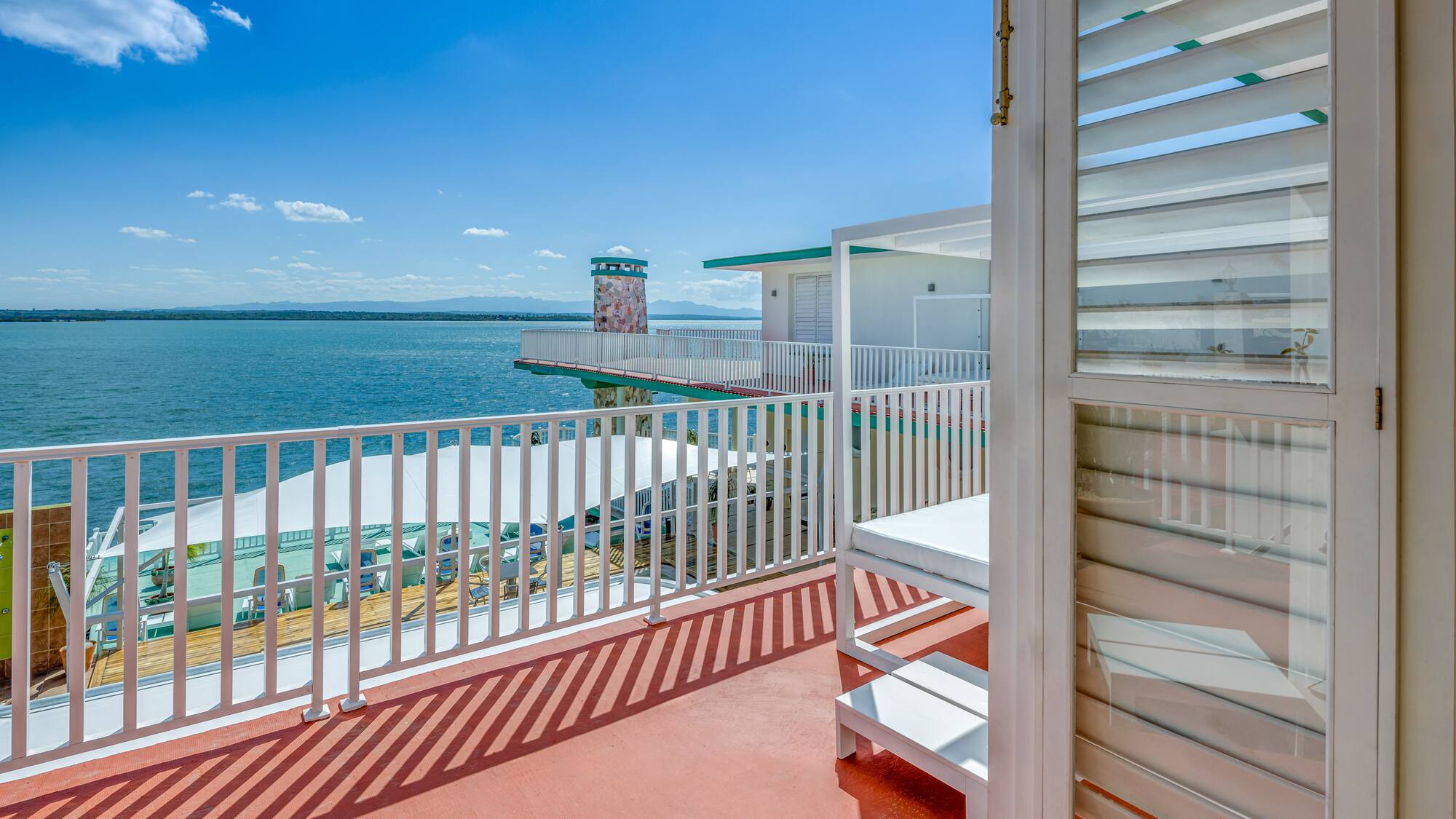 a deck with a white railing and a white building with a body of water in the background