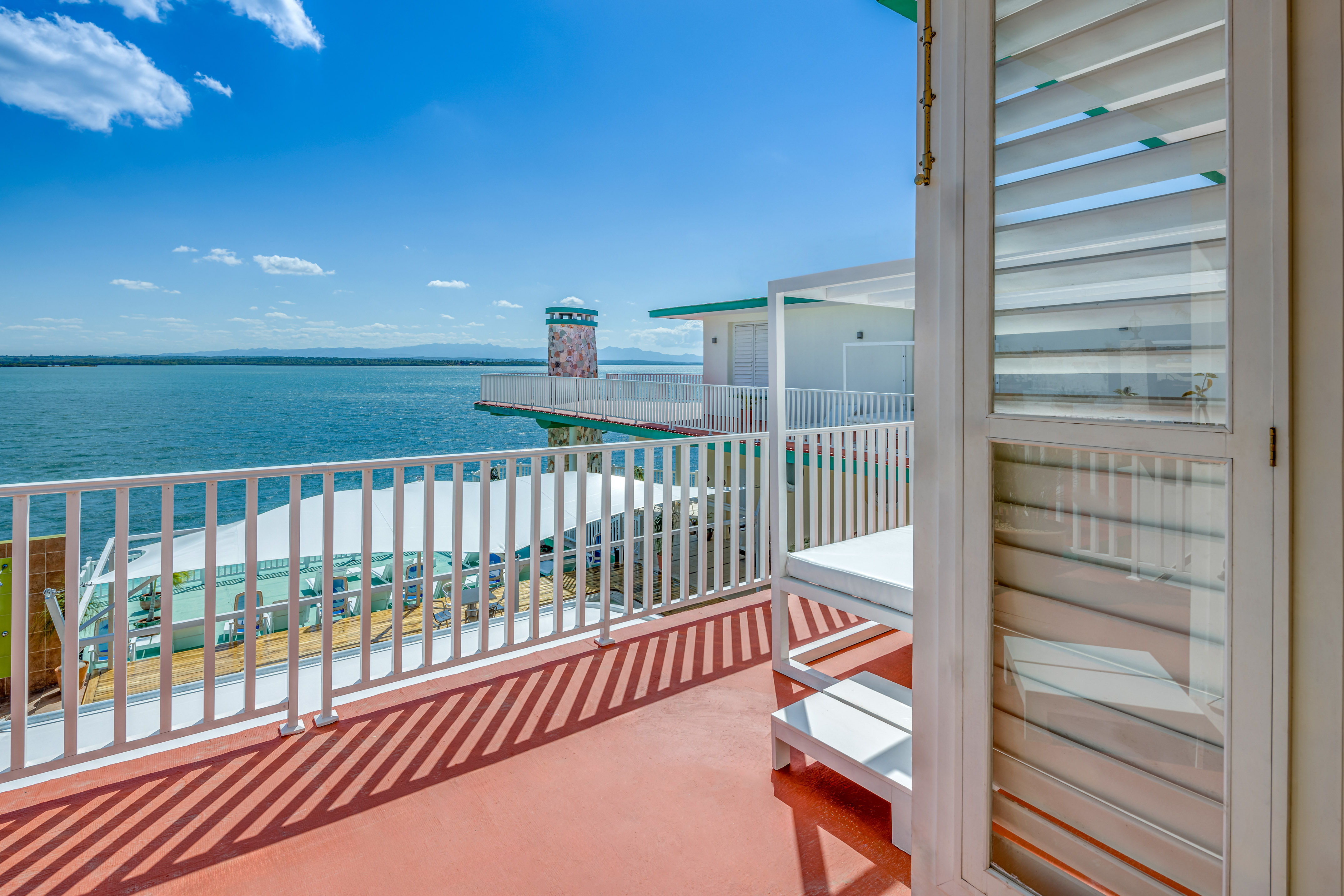 a deck with a white railing and a white building with a body of water in the background