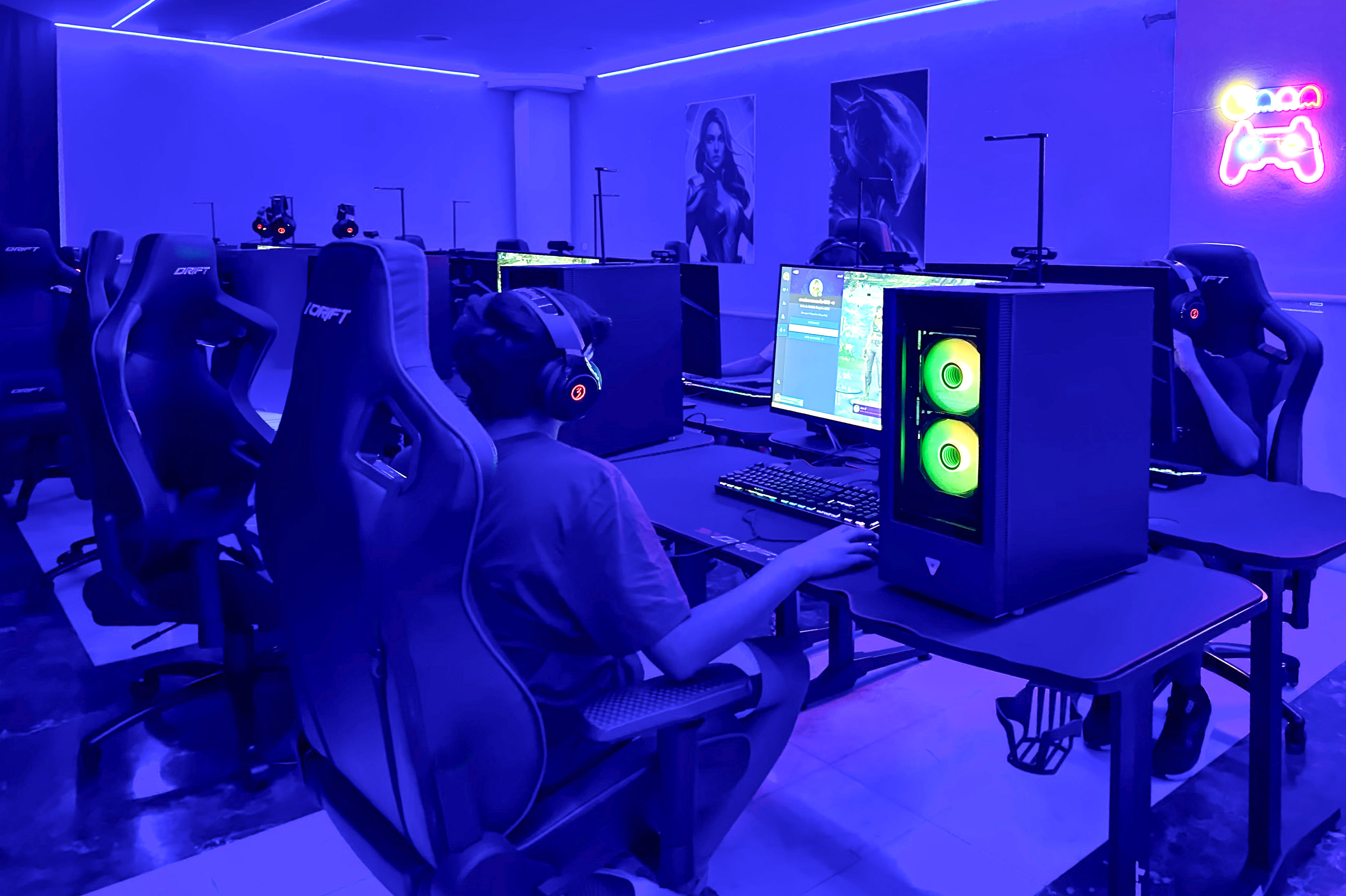 Esports arena with blue lighting, a gamer at a PC, and neon sign.