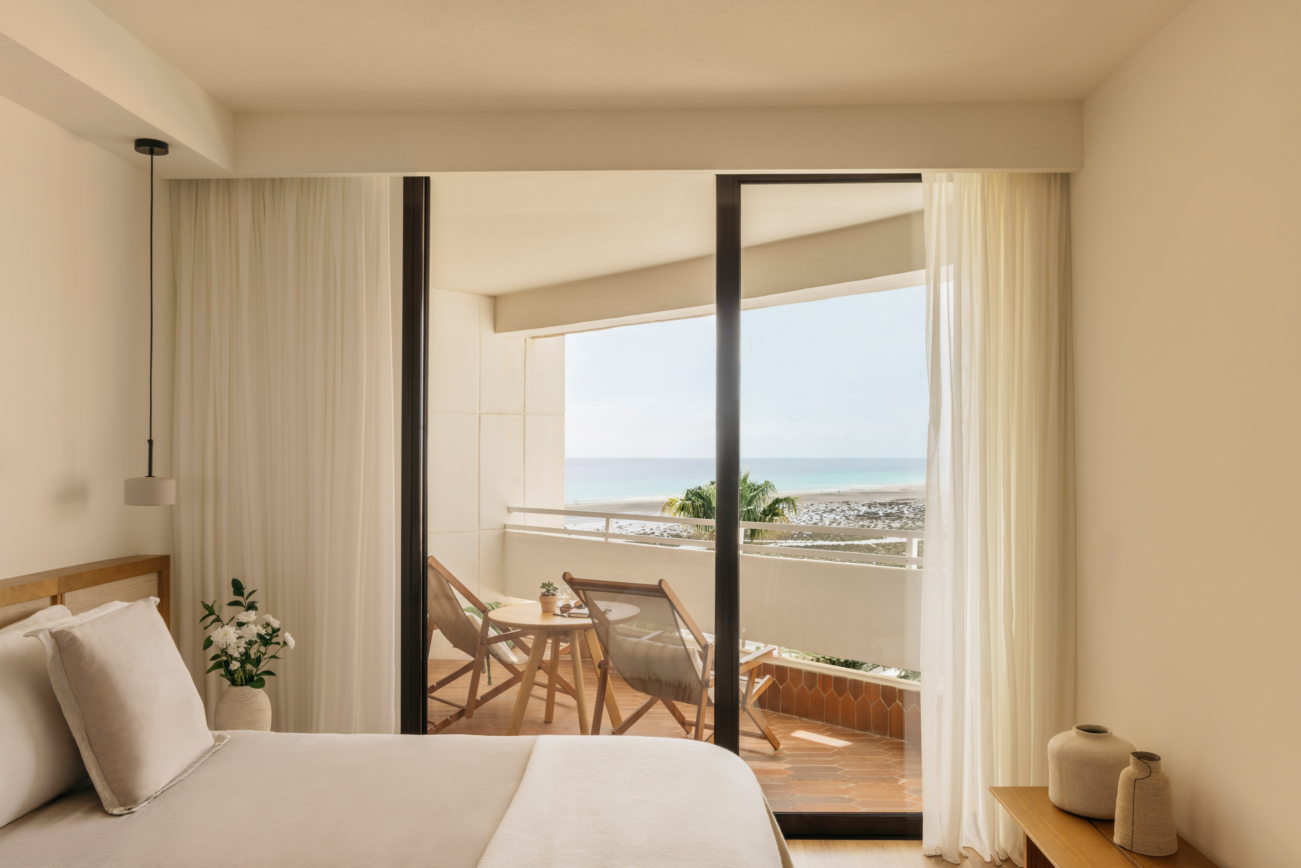 Modern hotel bedroom with ocean view balcony overlooking a sunny beach.