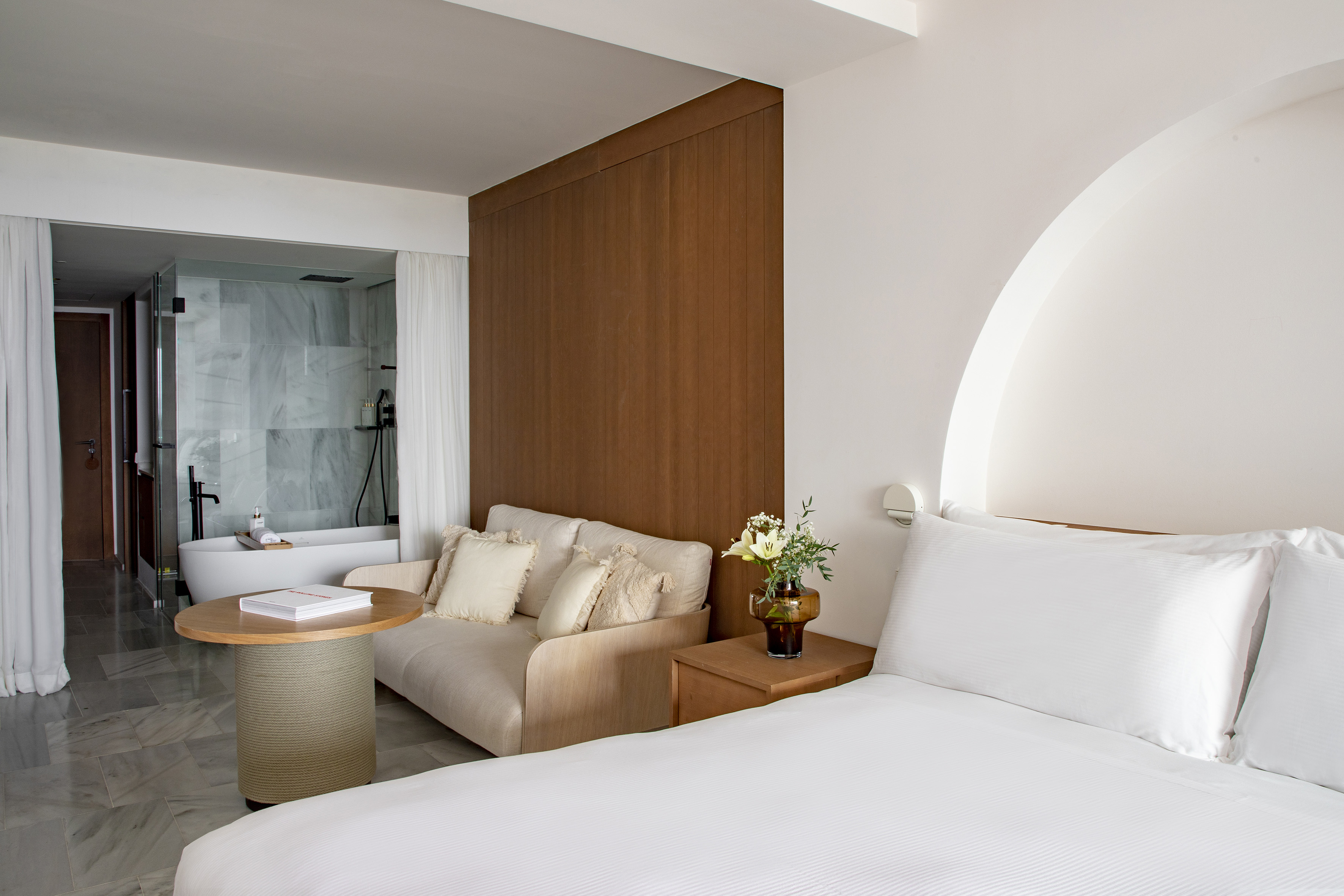 Contemporary hotel room with bed, lounge area, and freestanding bathtub.