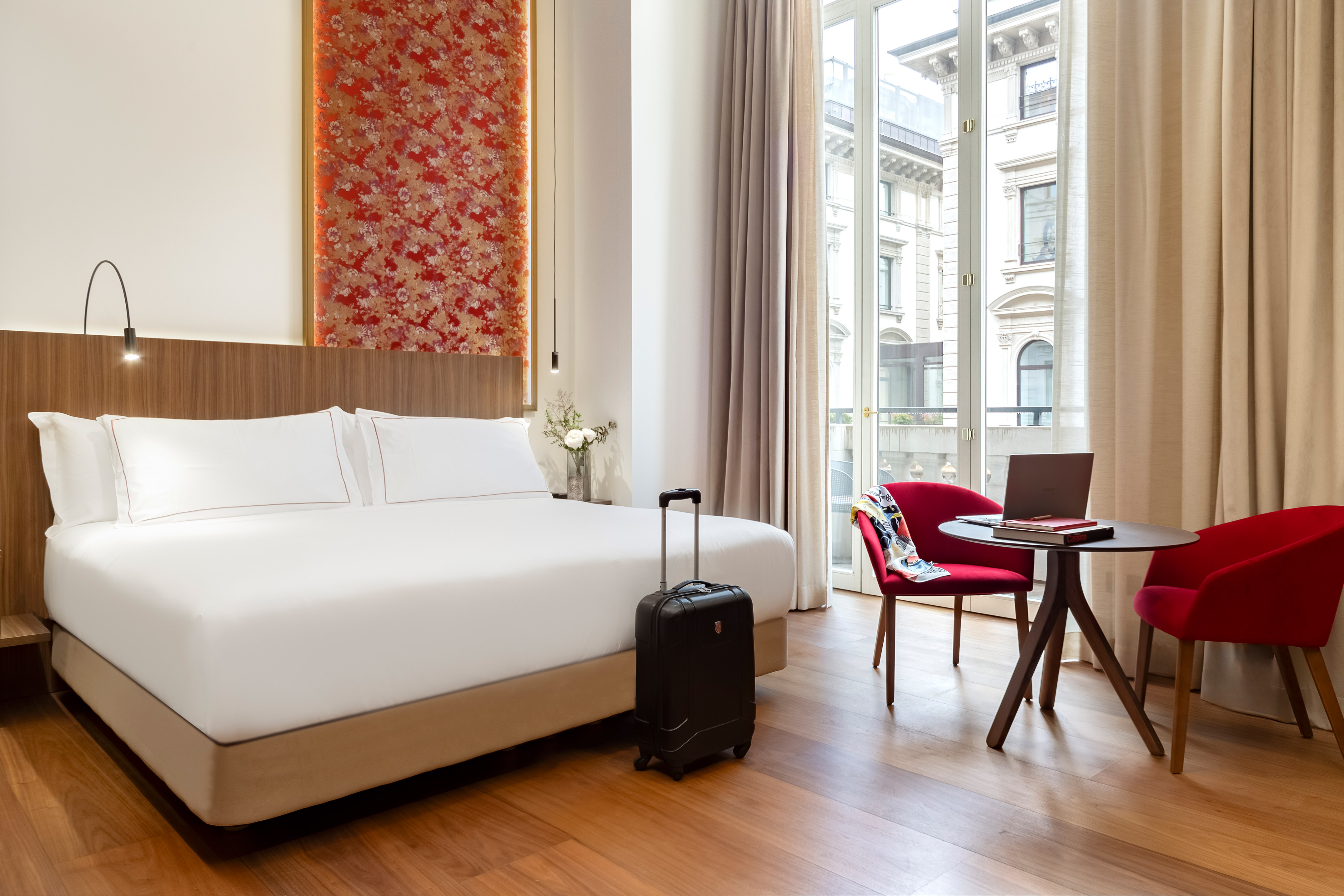 Spacious hotel room with king bed, modern decor, workstation, and city balcony view.