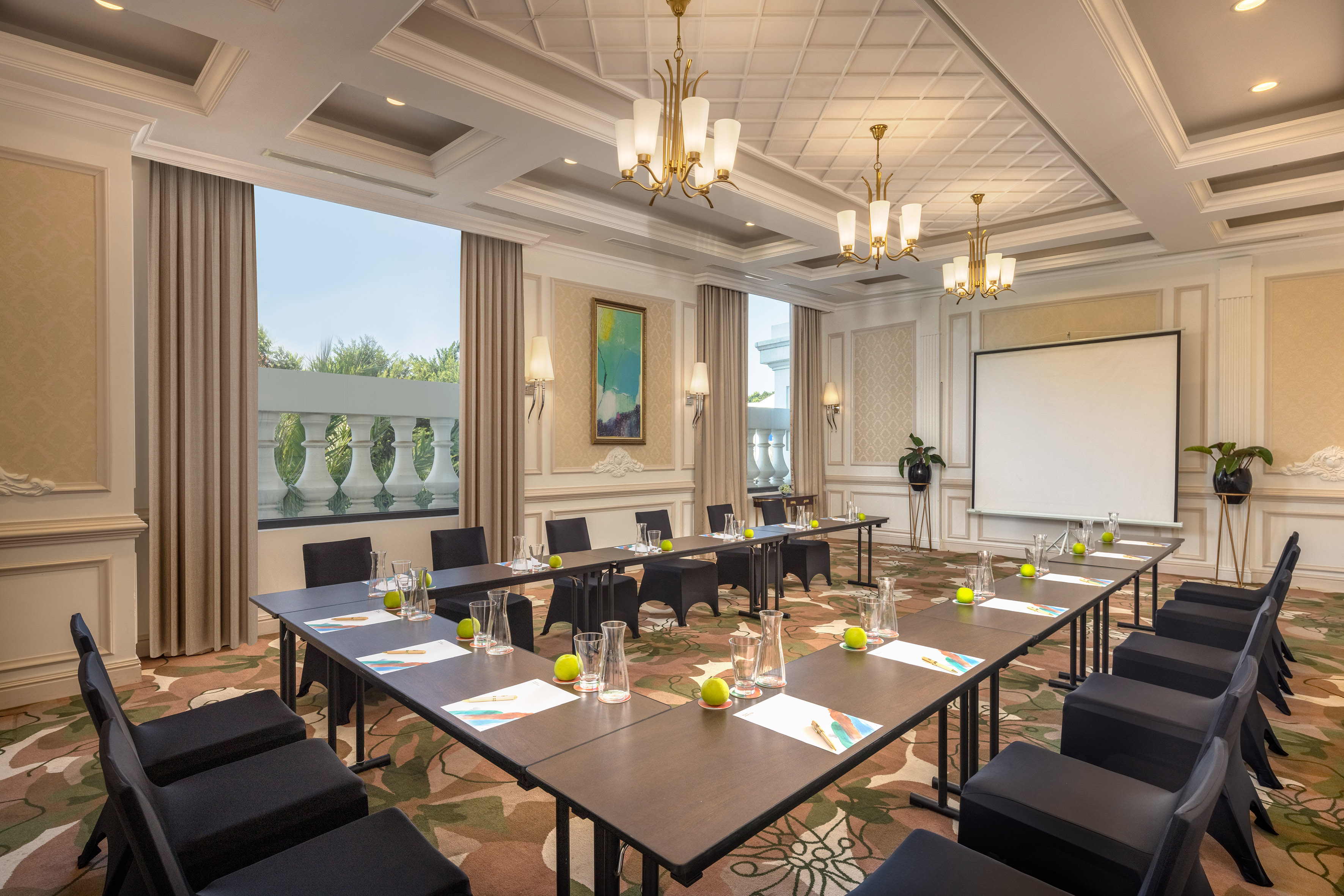 Elegant U-shaped conference room with projector screen and chandeliers.