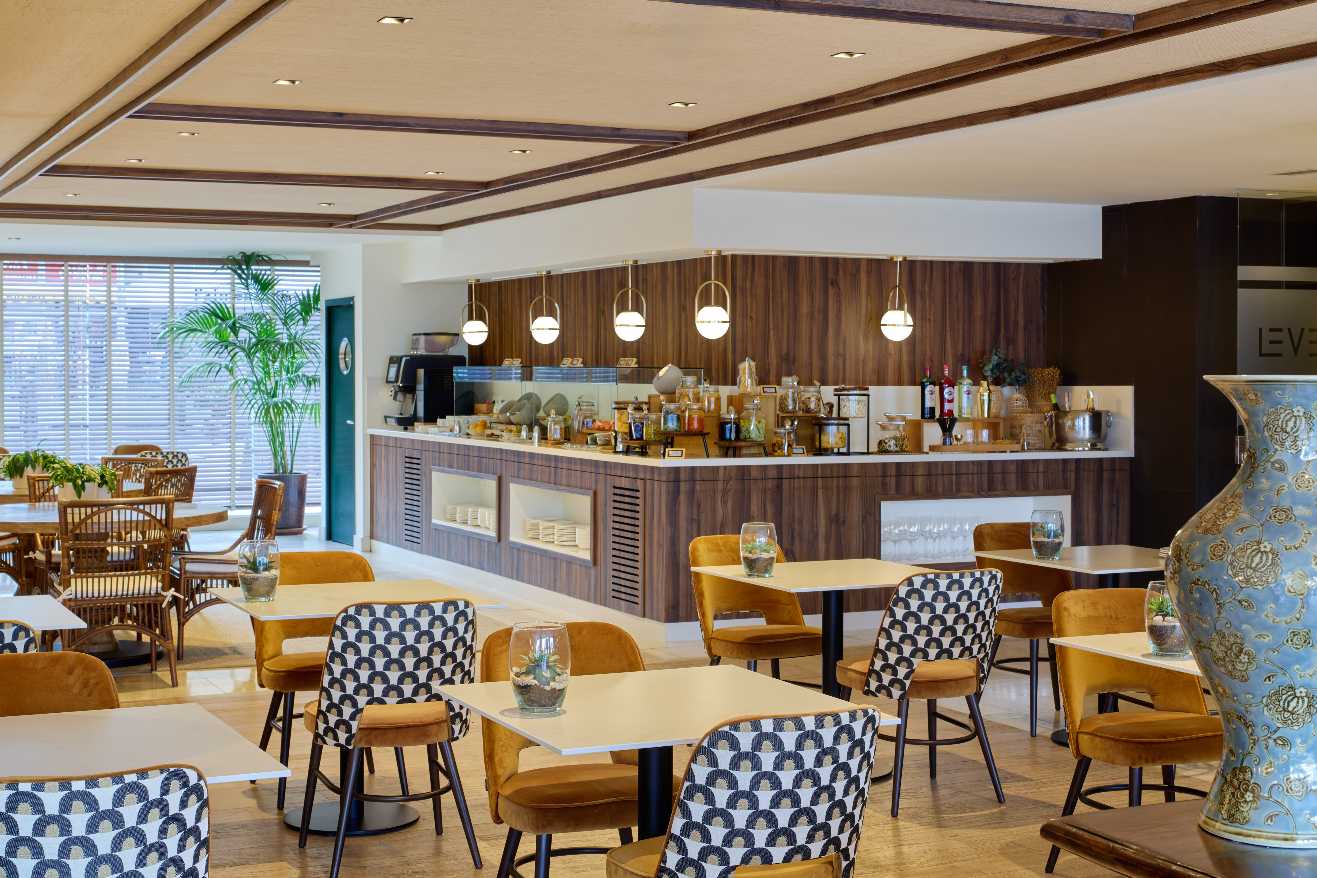 Hotel breakfast buffet with modern dining area, warm wood, and stylish gold chairs.