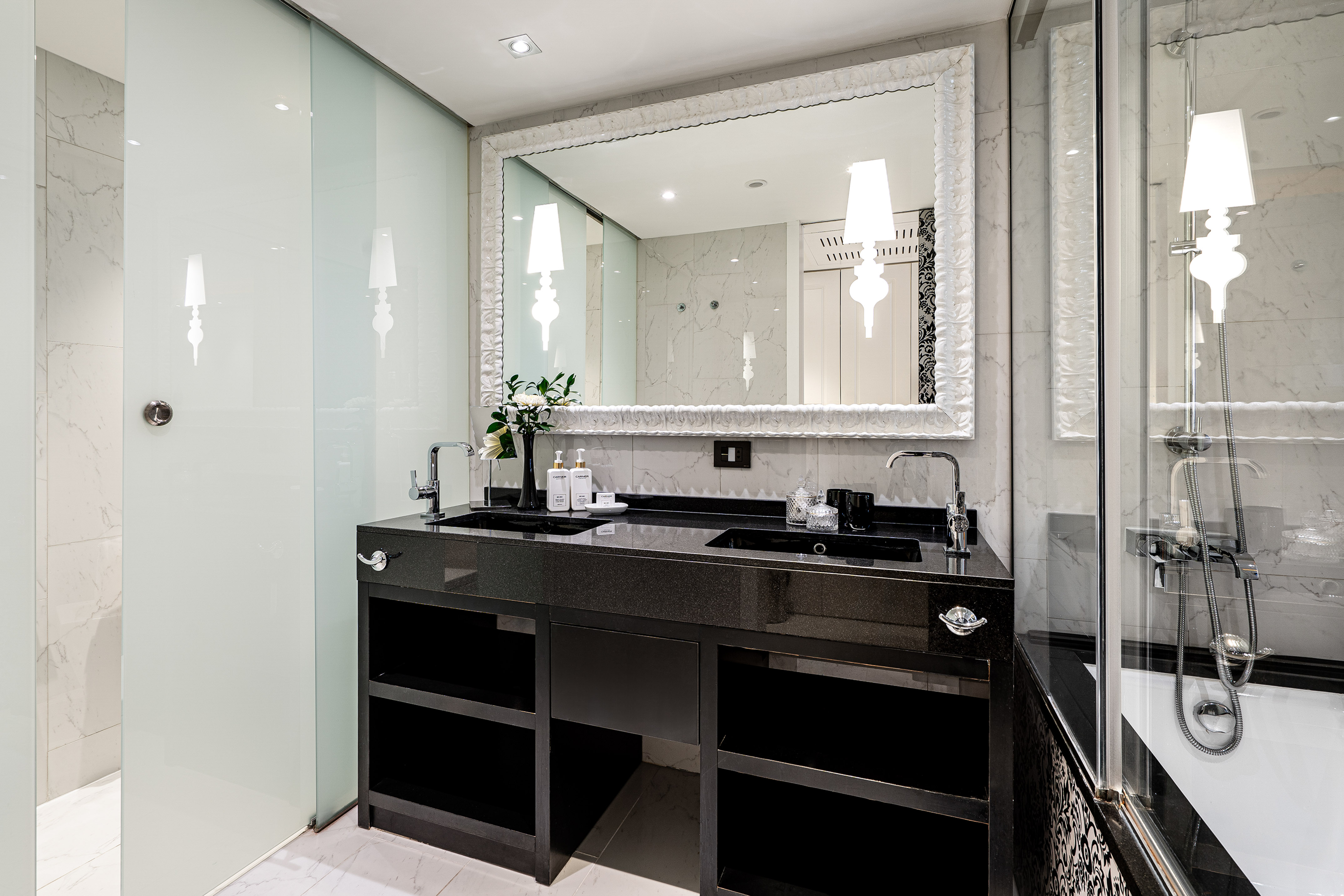 Luxury bathroom with black double vanity, marble, ornate mirror, glass shower.