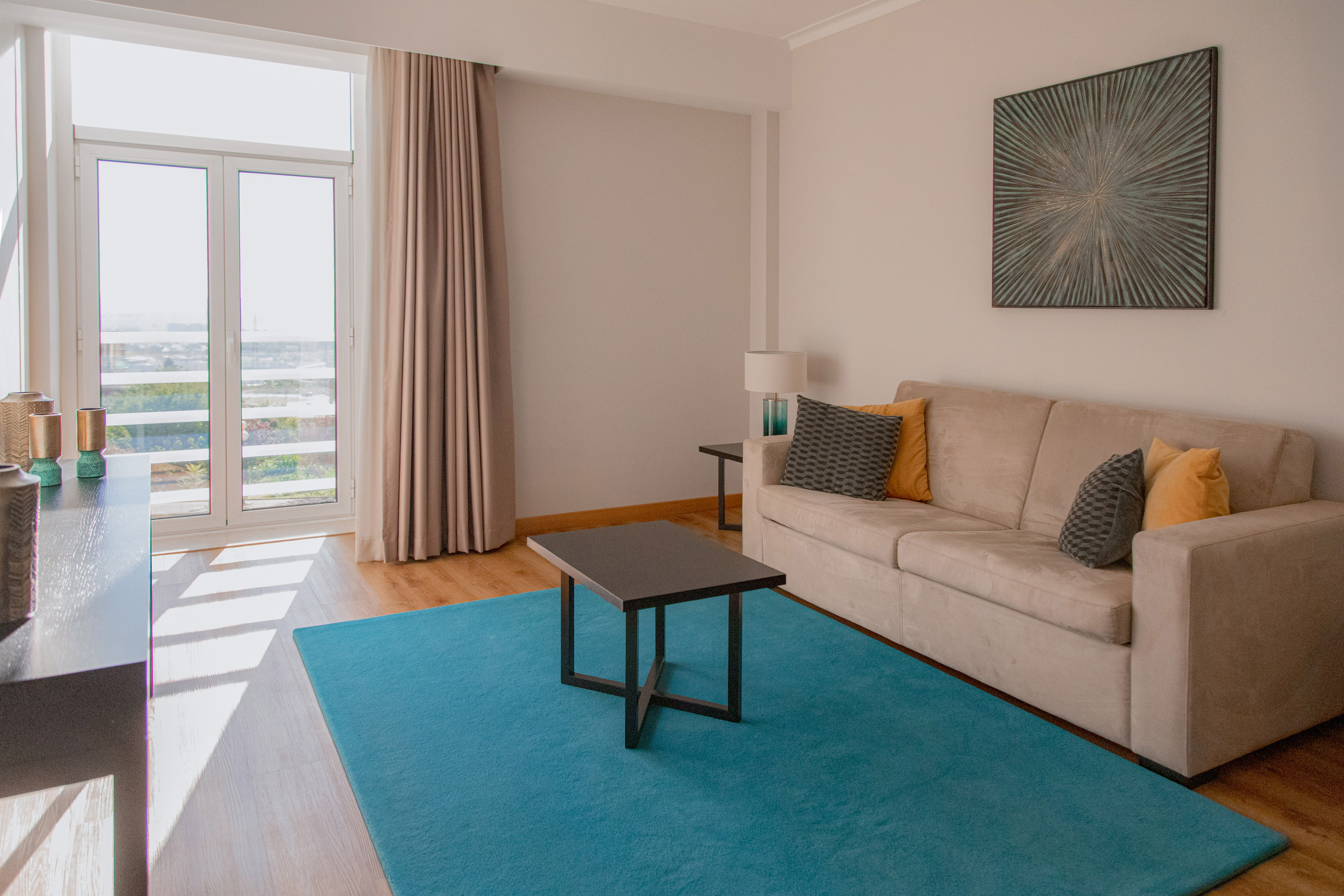 Living room with beige sofa, teal rug, coffee table, and bright window.
