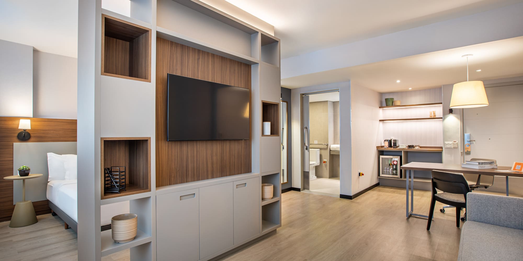 Modern hotel studio suite with bedroom, TV wall, and dedicated workspace.