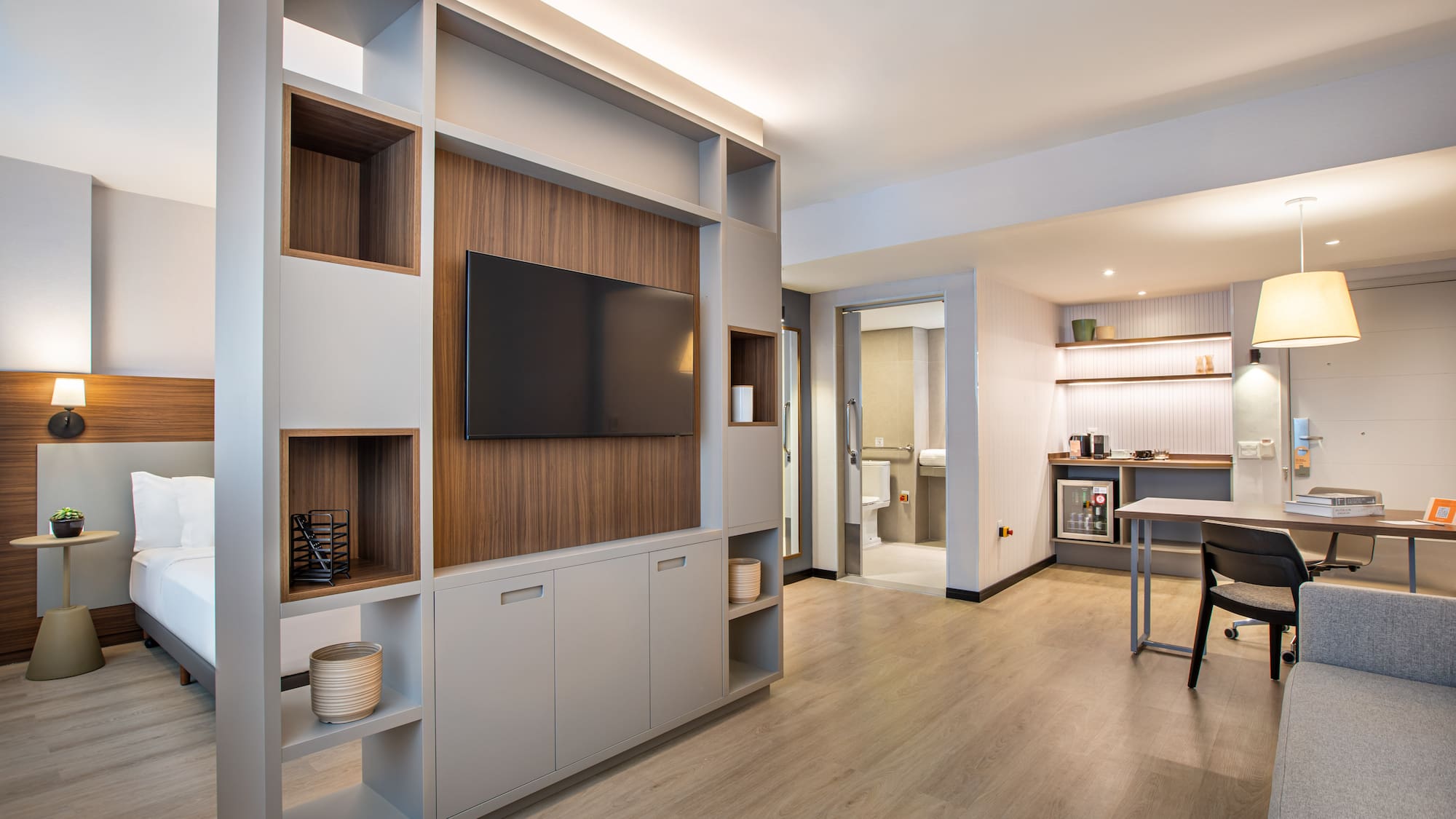 Modern hotel studio suite with bedroom, TV wall, and dedicated workspace.