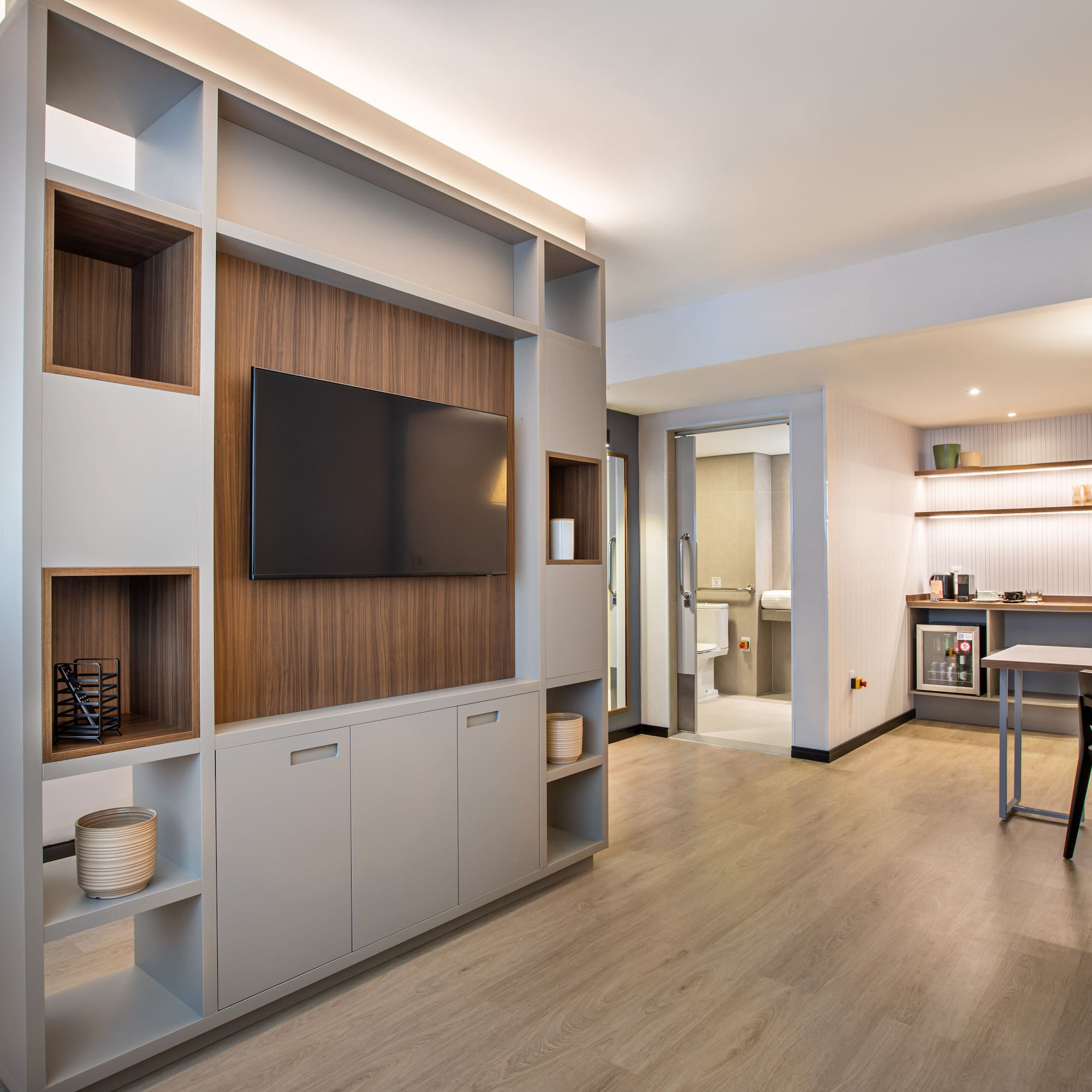 Modern hotel studio suite with bedroom, TV wall, and dedicated workspace.