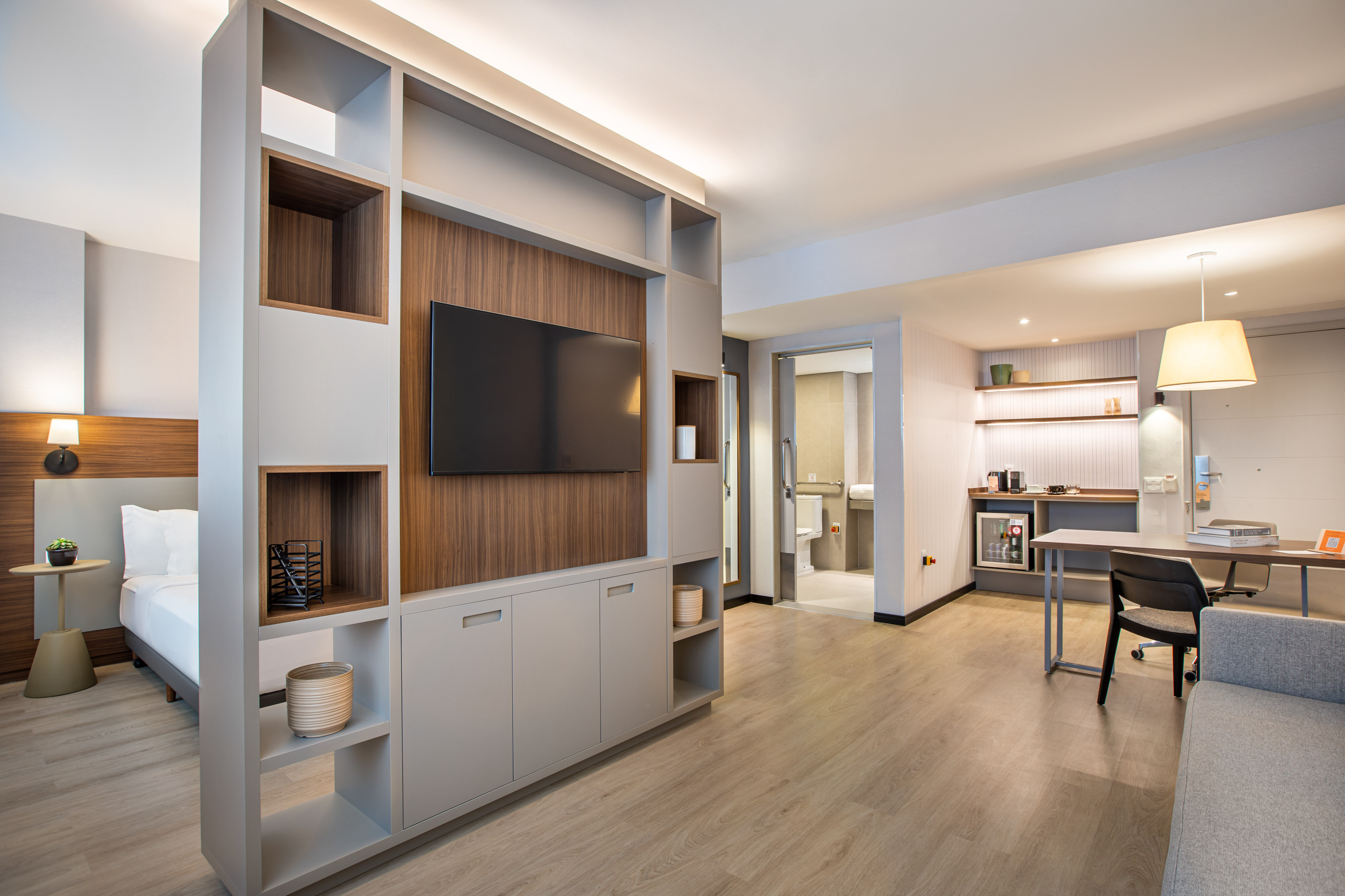 Modern hotel studio suite with bedroom, TV wall, and dedicated workspace.