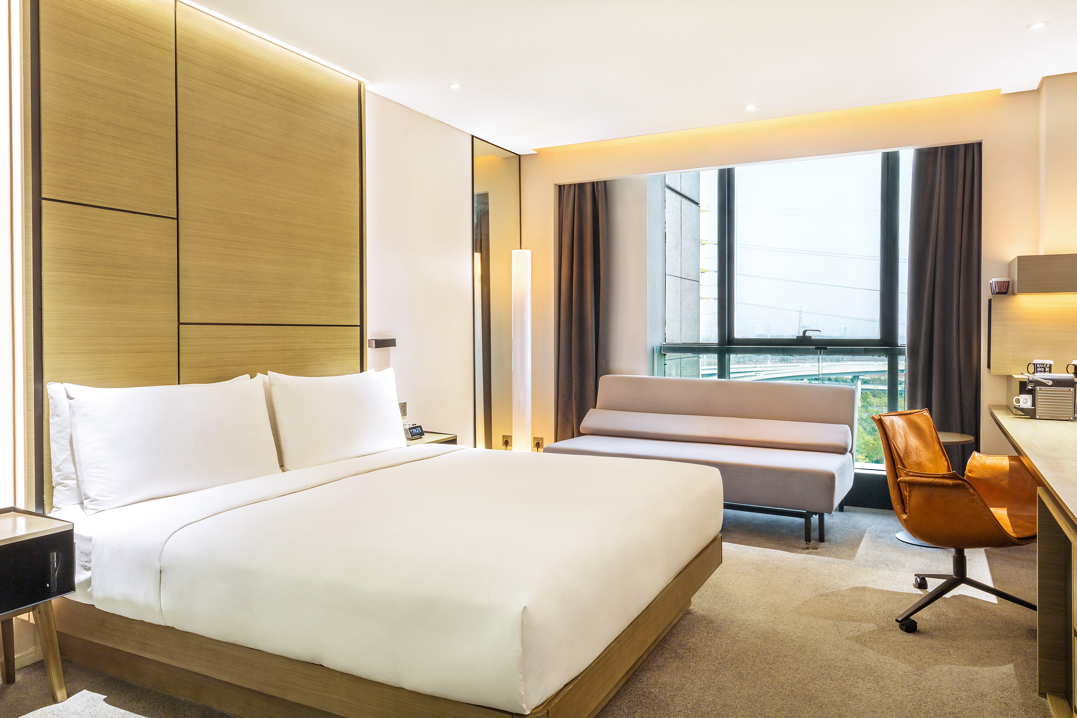 Modern hotel room with king bed, city view, desk, and brown leather chair.