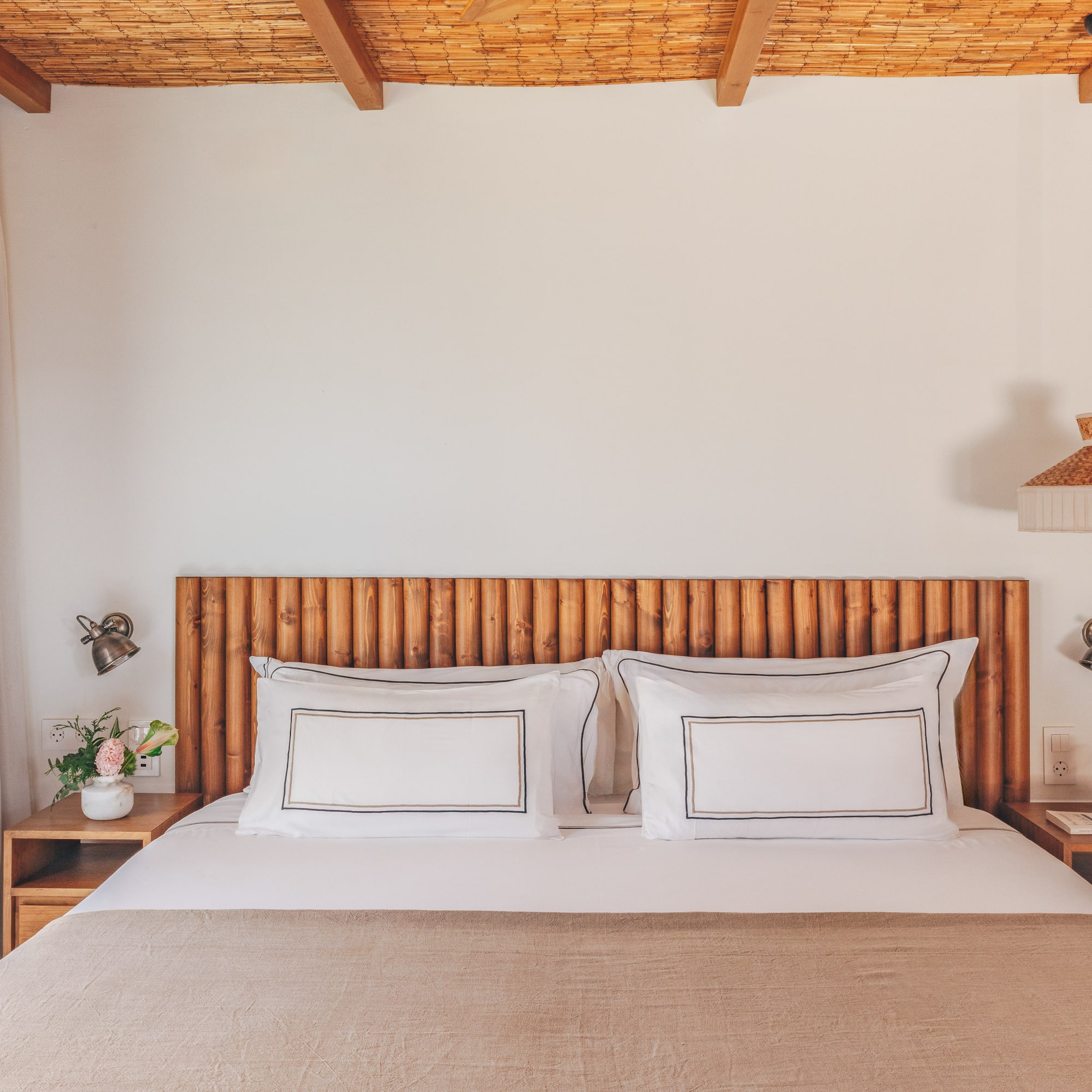 Cozy bedroom with wooden headboard, bamboo ceiling, white bed, and natural decor.