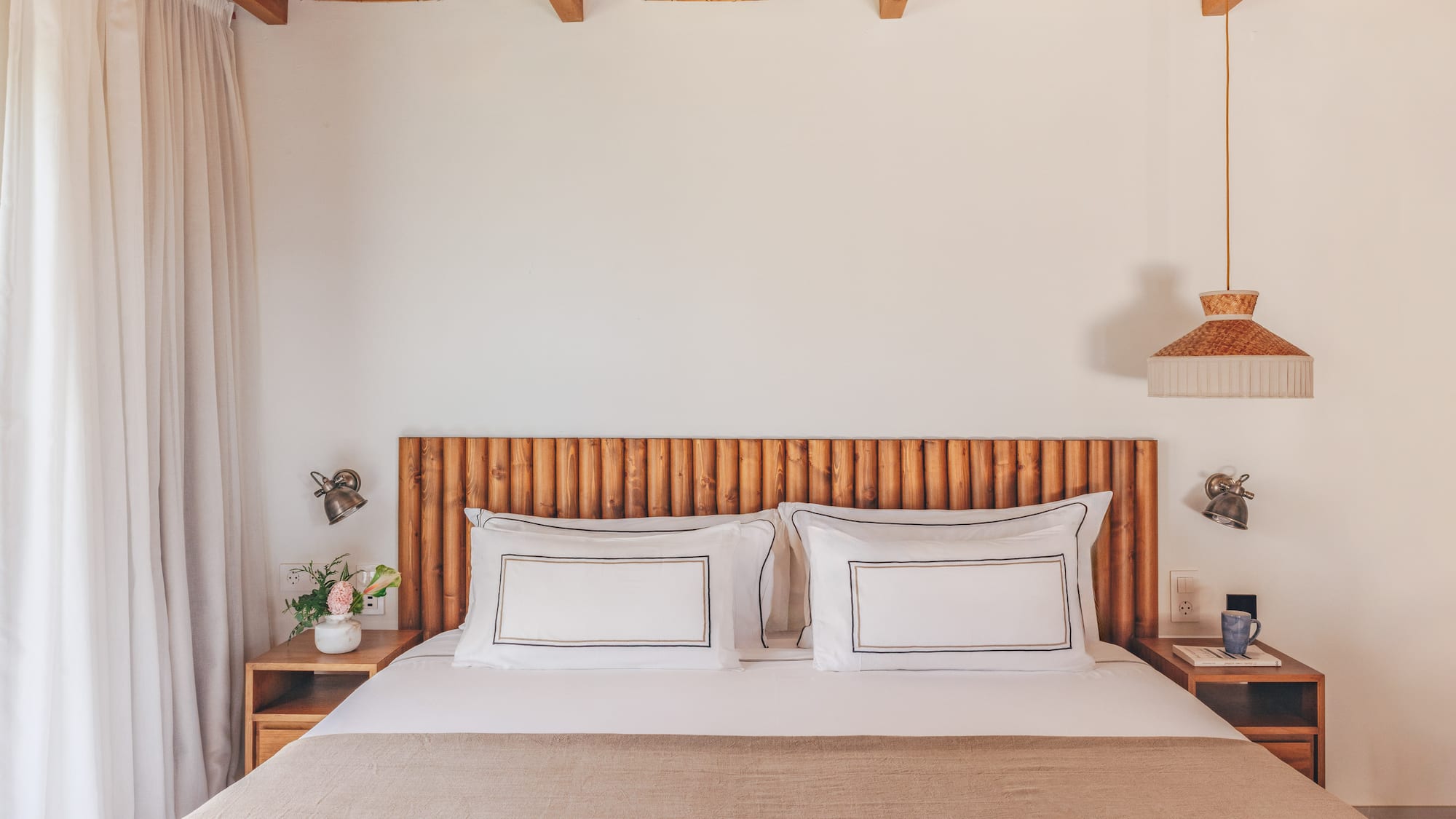Cozy bedroom with wooden headboard, bamboo ceiling, white bed, and natural decor.