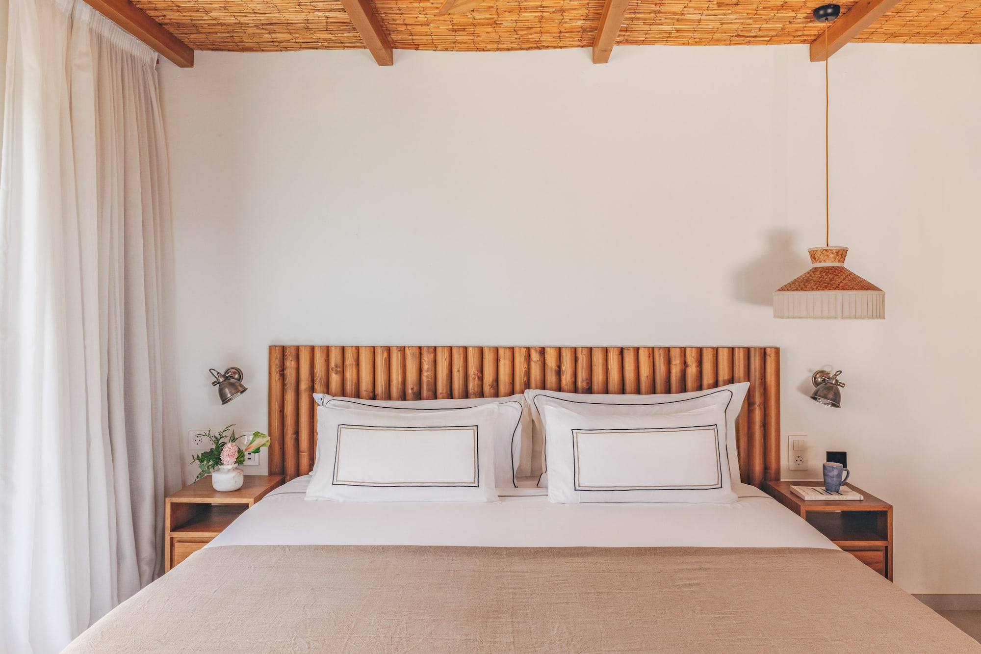 Cozy bedroom with wooden headboard, bamboo ceiling, white bed, and natural decor.