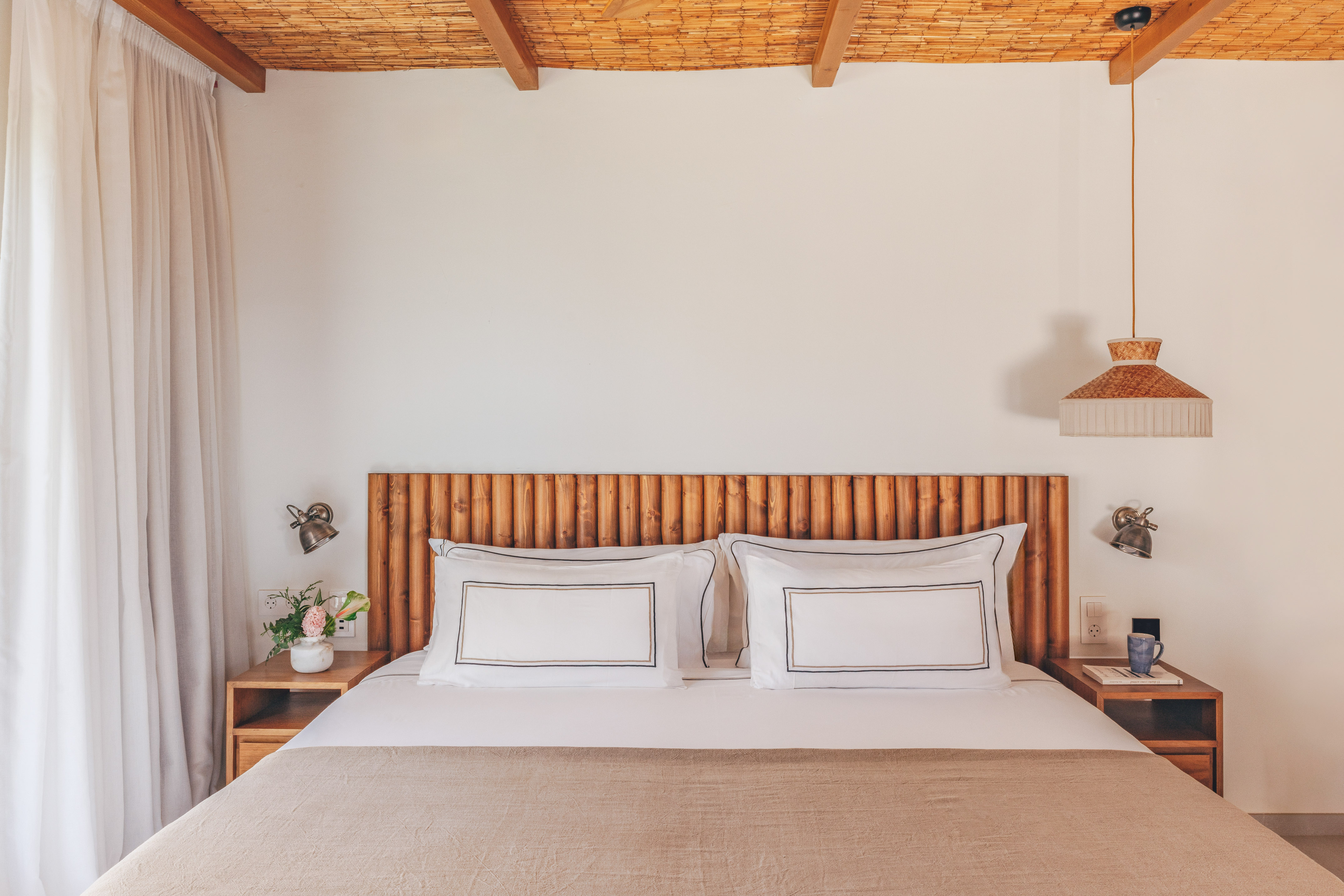 Cozy bedroom with wooden headboard, bamboo ceiling, white bed, and natural decor.