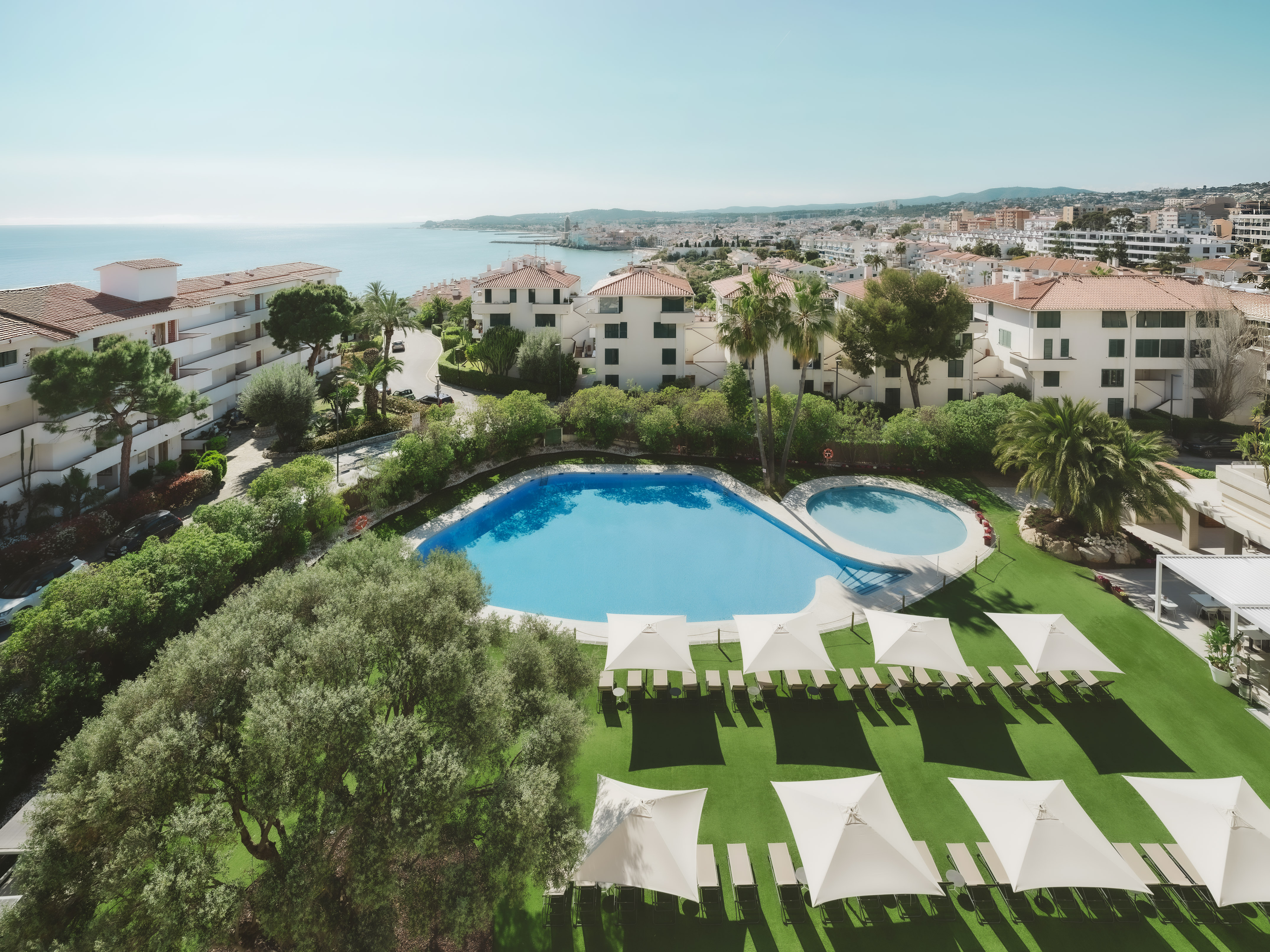 Sunny Mediterranean resort with two pools, lounge chairs, and ocean view.