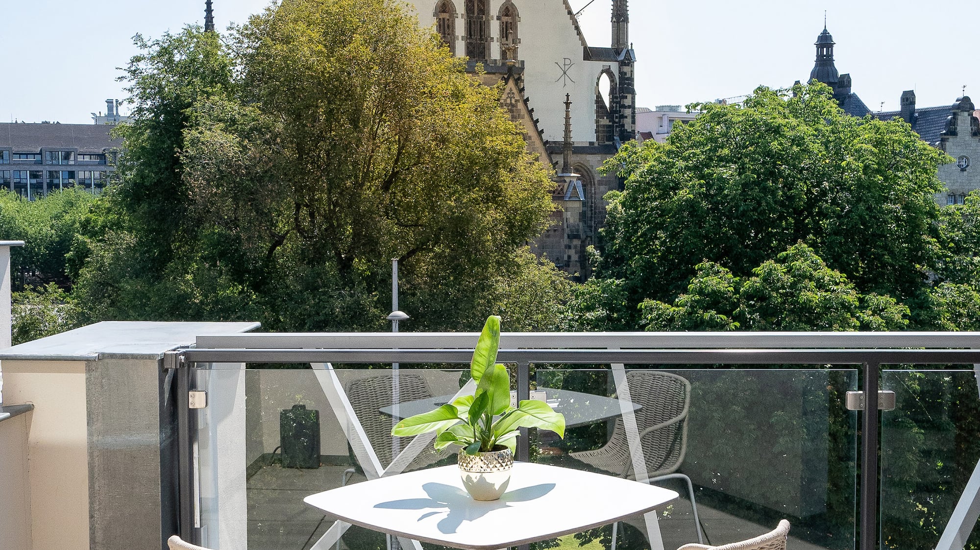 Sunny balcony with outdoor furniture, potted plant, and historic church view.