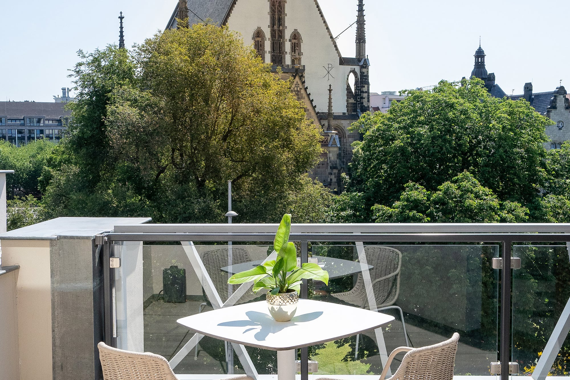 Sunny balcony with outdoor furniture, potted plant, and historic church view.