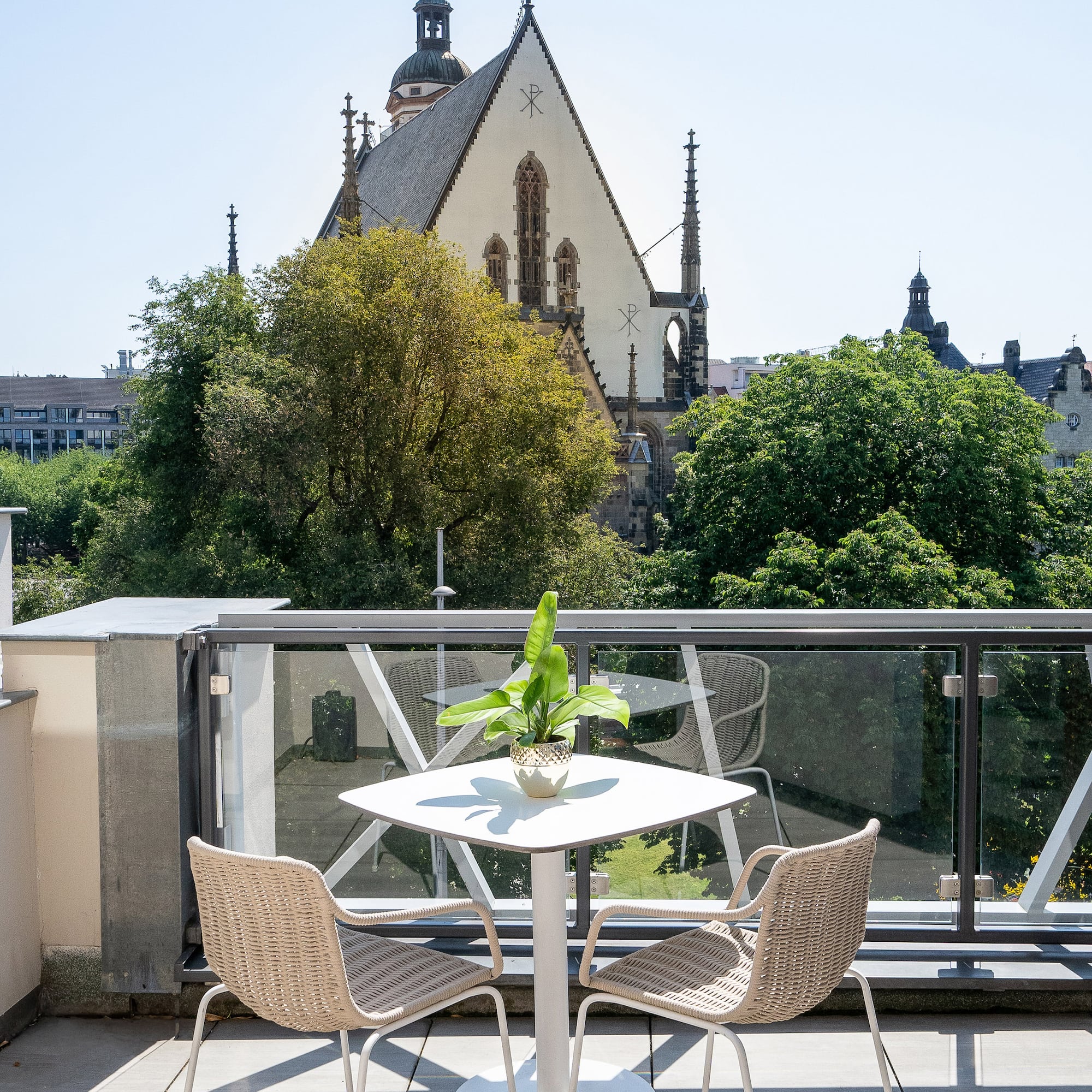 Sunny balcony with outdoor furniture, potted plant, and historic church view.