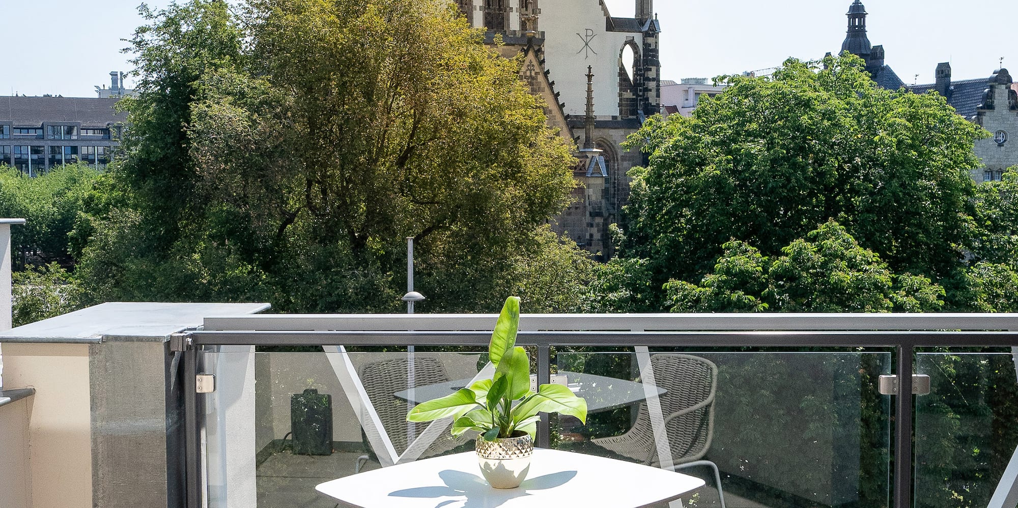 Sunny balcony with outdoor furniture, potted plant, and historic church view.