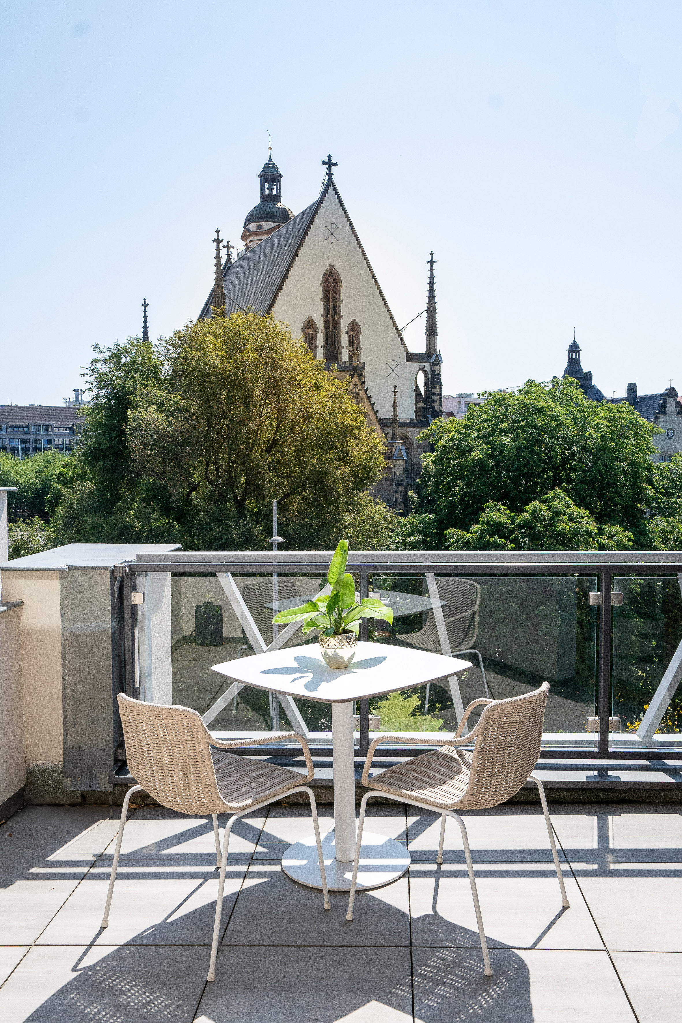 Sunny balcony with outdoor furniture, potted plant, and historic church view.
