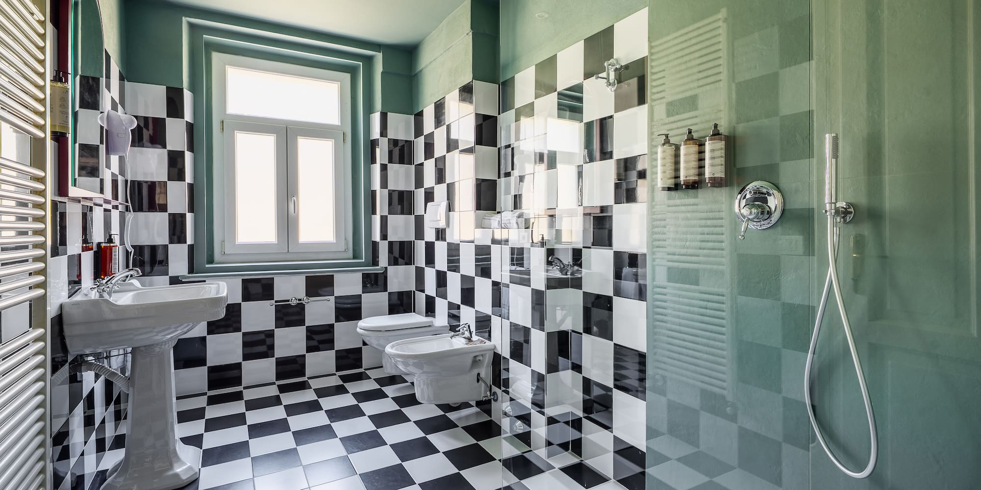Checkered tile bathroom with green walls, pedestal sink, toilet, and shower.