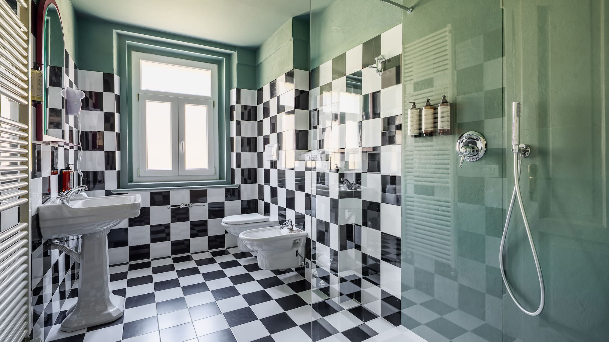 Stylish bathroom with black-white checkered tiles, green walls, pedestal sink, shower.