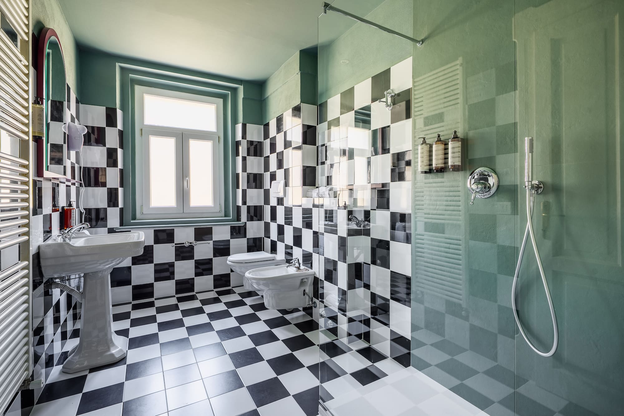 Checkered tile bathroom with green walls, pedestal sink, toilet, and shower.