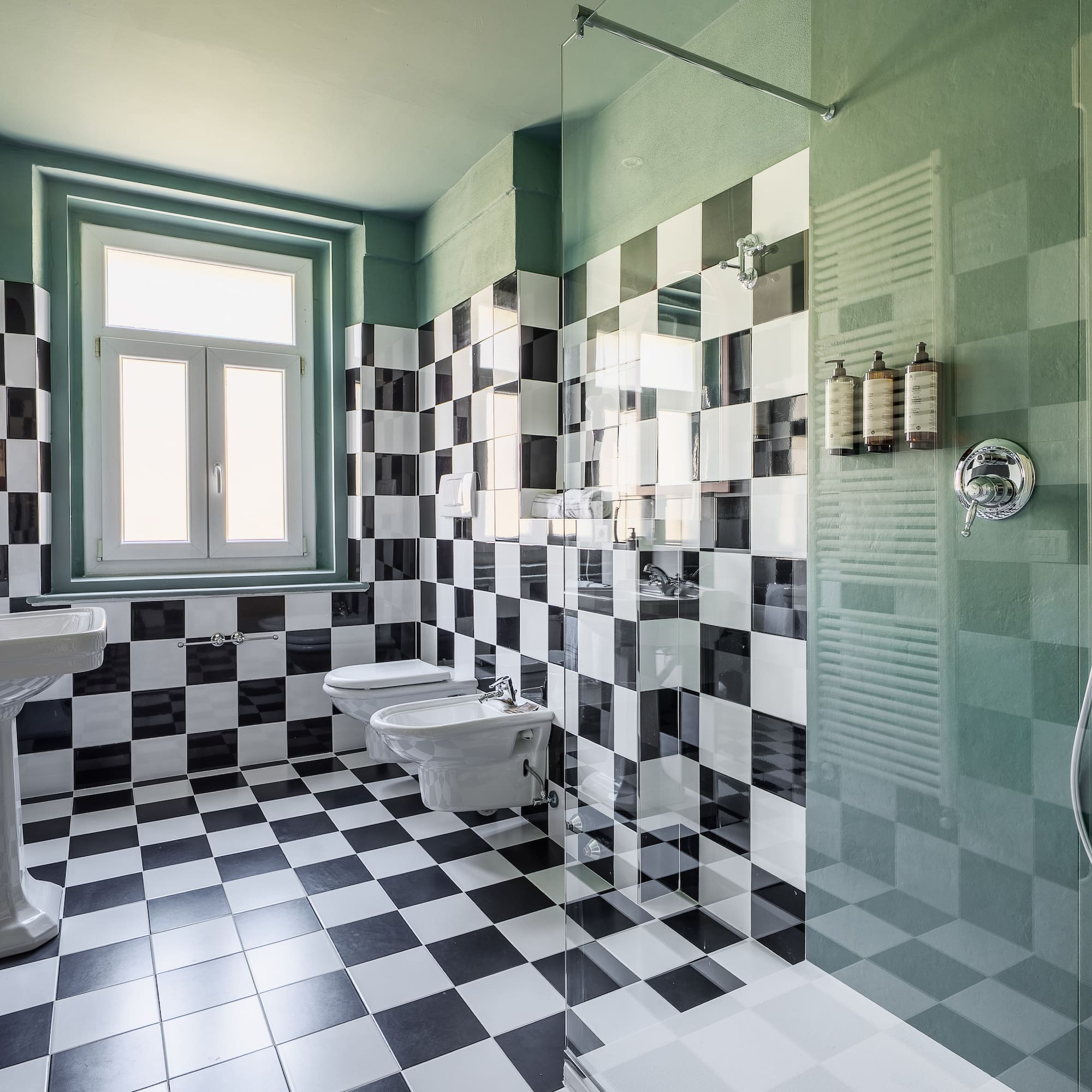 Checkered tile bathroom with green walls, pedestal sink, toilet, and shower.
