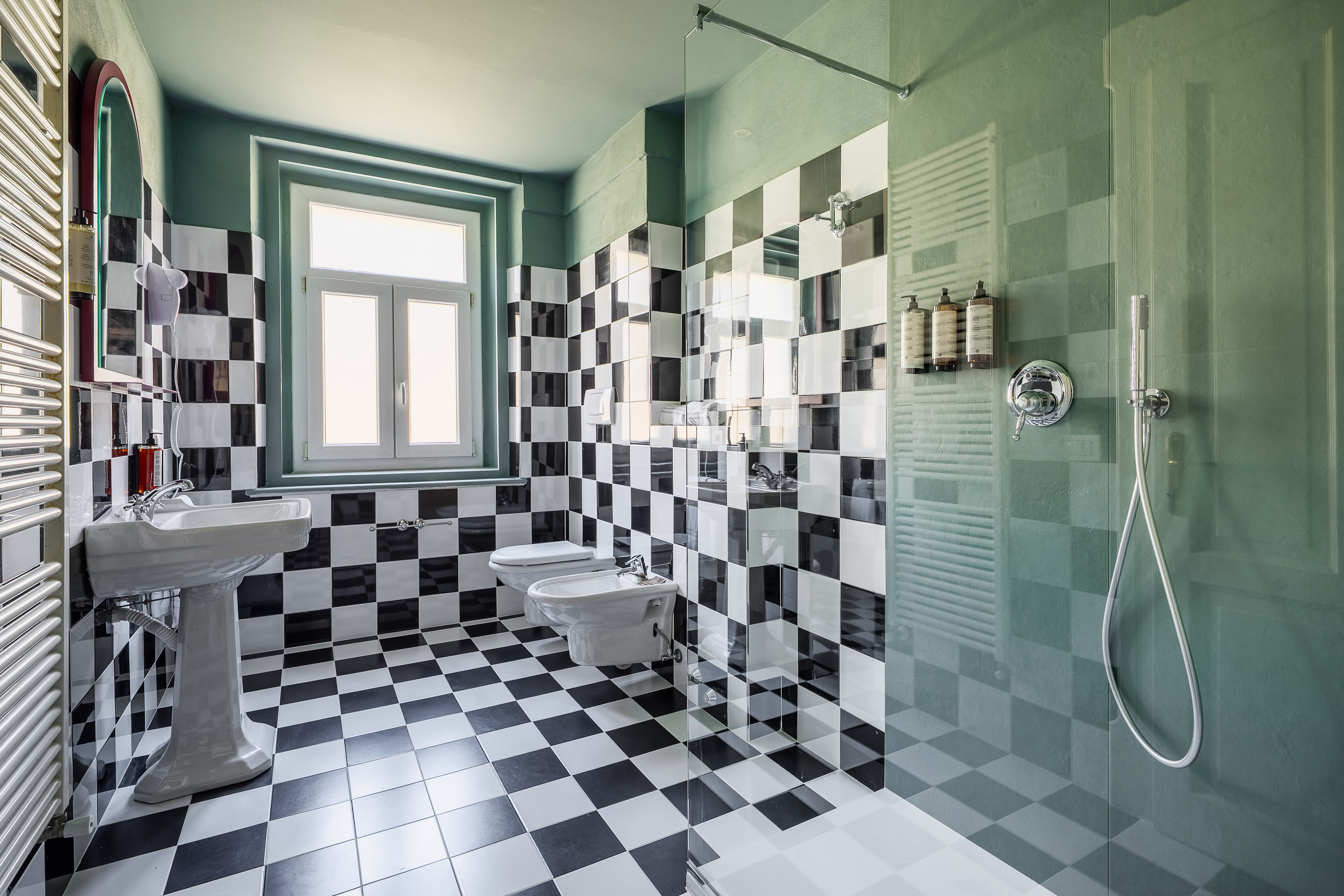 Checkered tile bathroom with green walls, pedestal sink, toilet, and shower.
