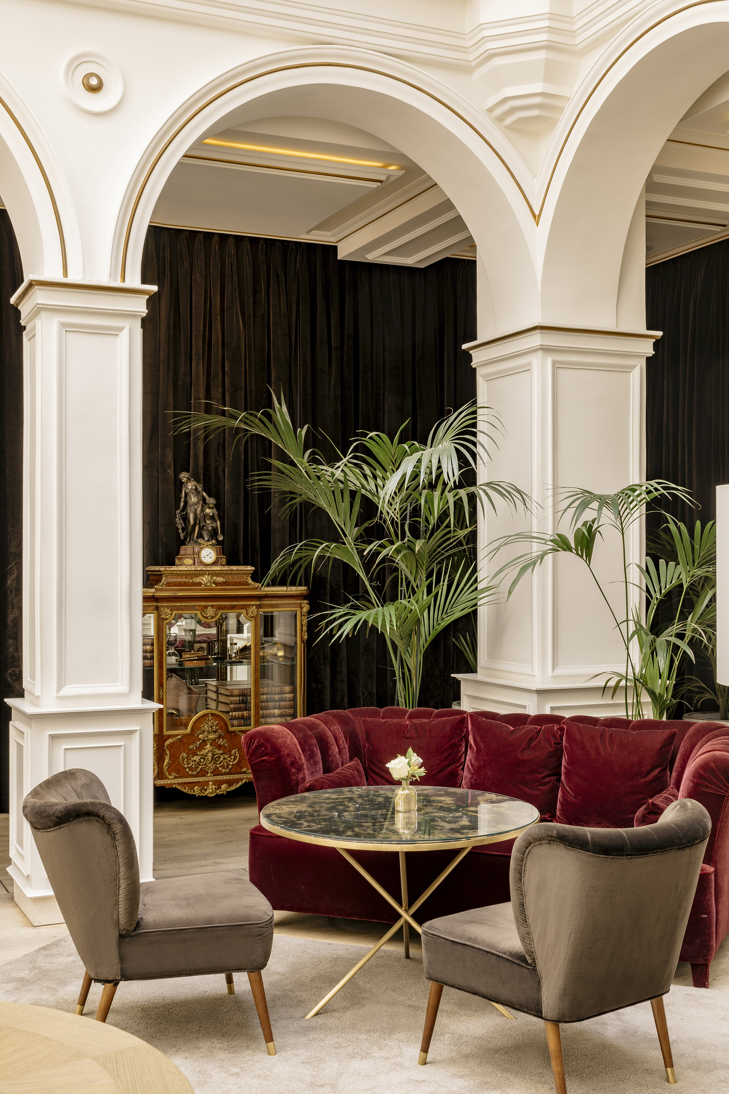 Elegant hotel lobby with red velvet sofa, classic arches, and ornate decor.