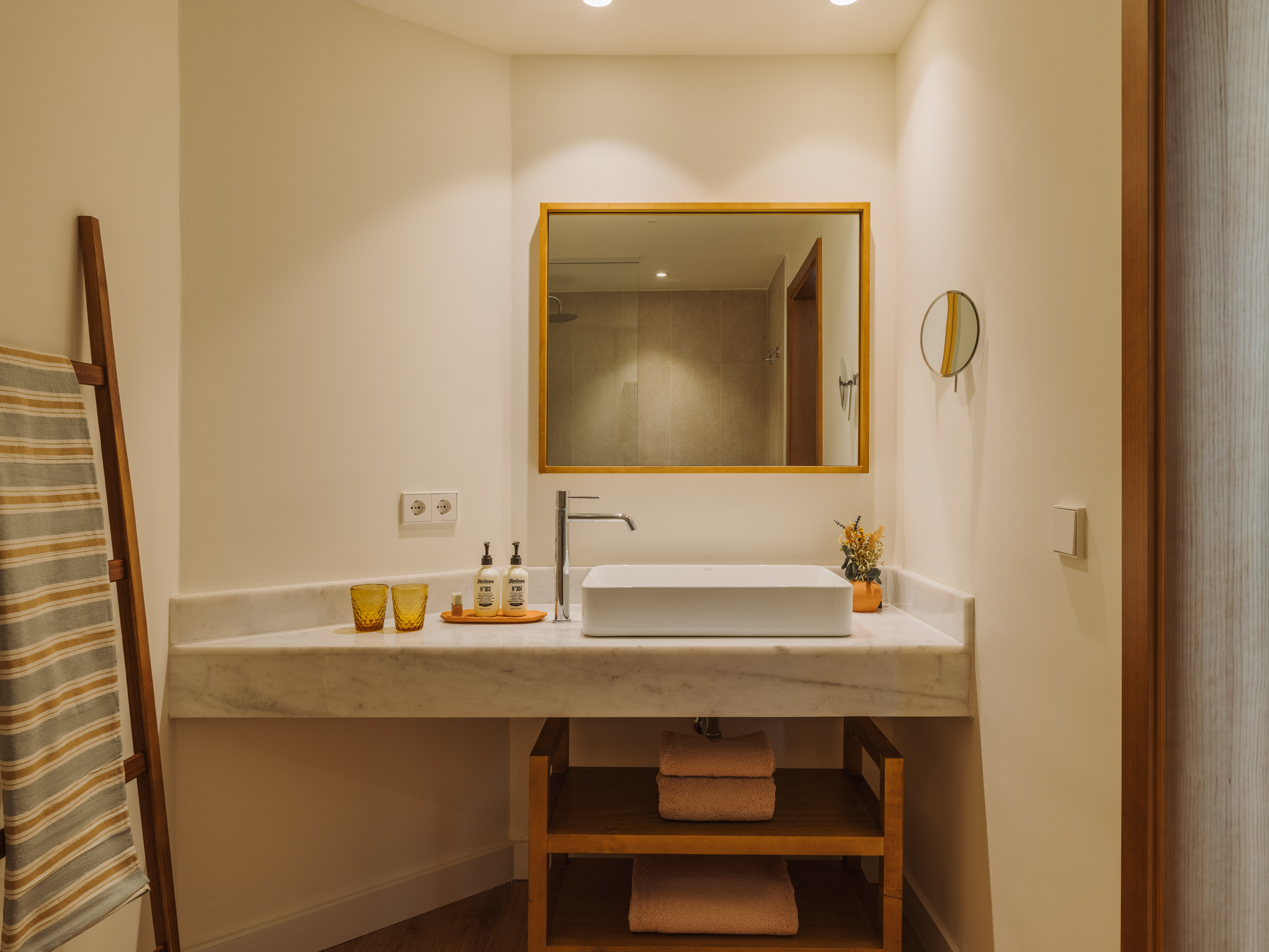 Modern hotel bathroom vanity with white sink, marble counter, wood mirror, and towels.