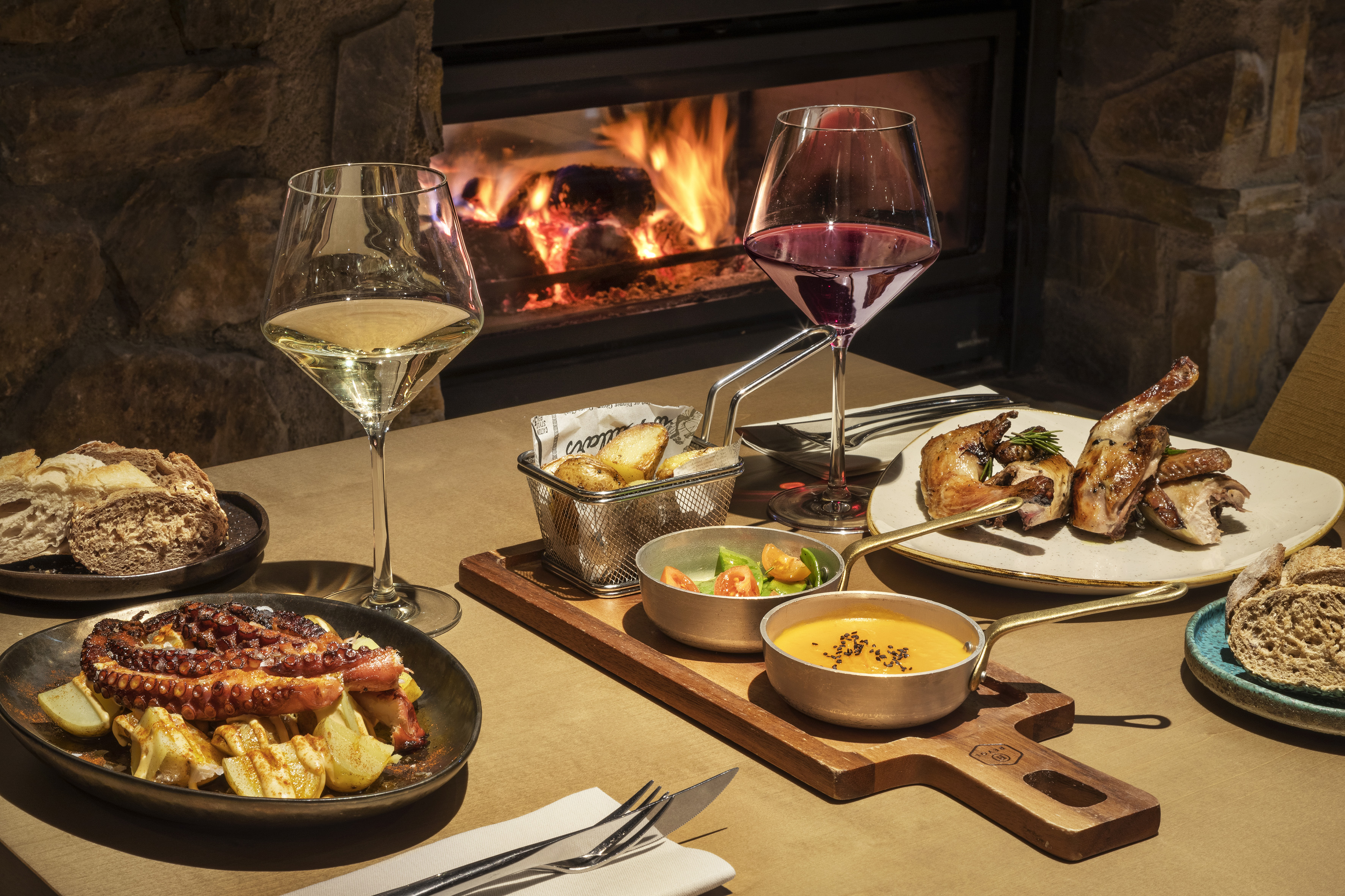 Cozy dinner with grilled octopus, roasted poultry, wine, and warm fireplace.