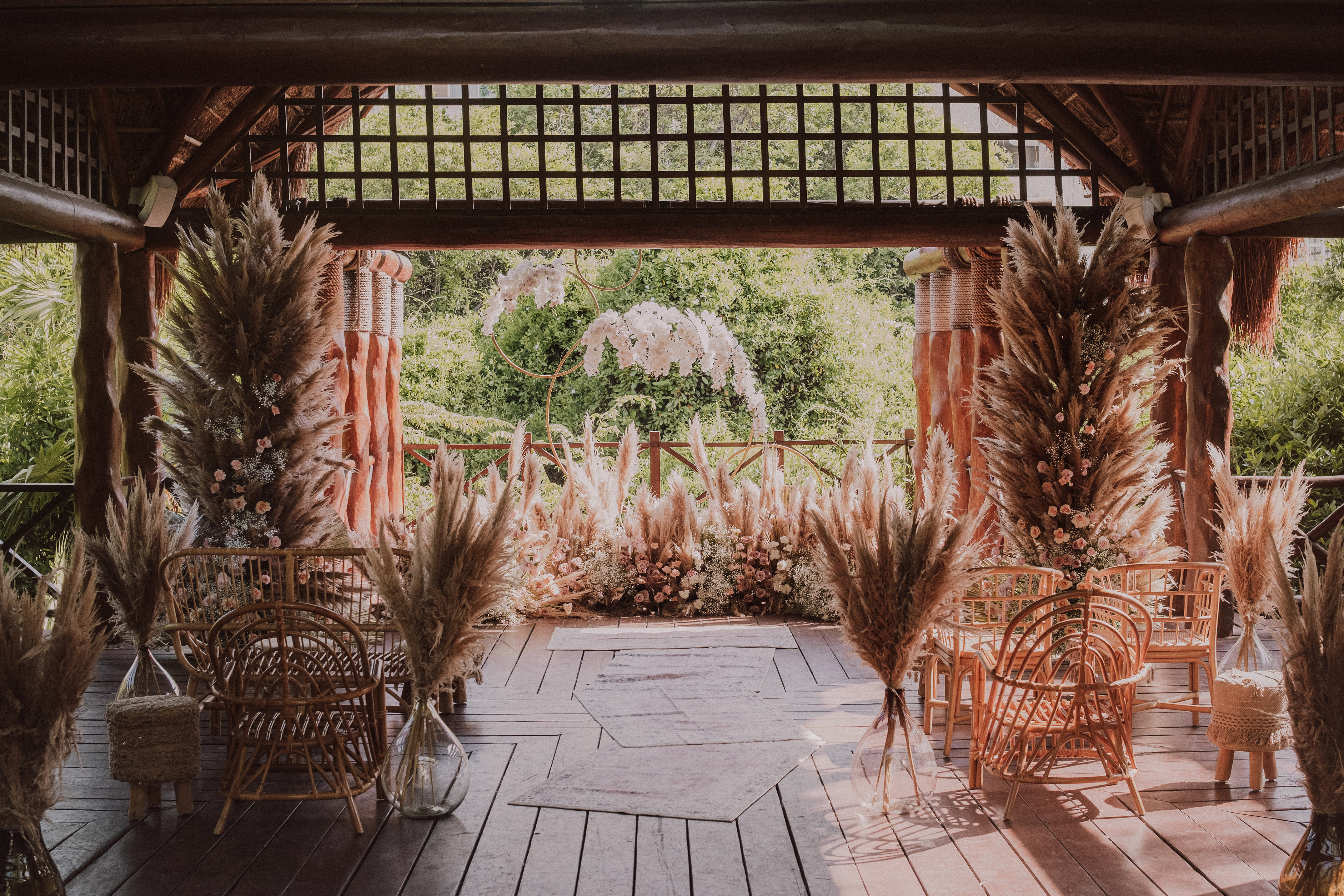 Boho wedding venue with pampas grass, flowers, and wicker chairs outdoors.