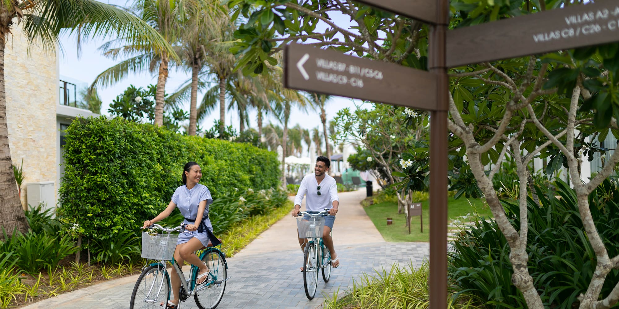a man and woman riding bicycles on a path with trees and bushes