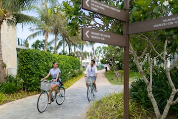 a man and woman riding bicycles on a path with trees and bushes