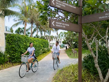 a man and woman riding bicycles on a path with trees and bushes
