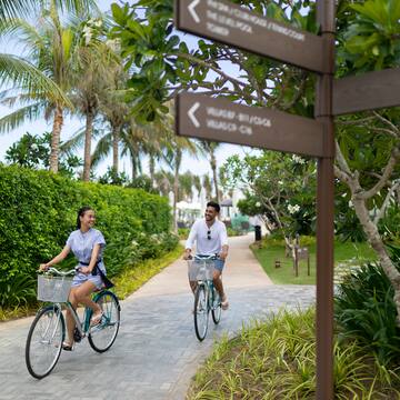 a man and woman riding bicycles on a path with trees and bushes