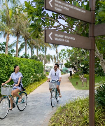a man and woman riding bicycles on a path with trees and bushes