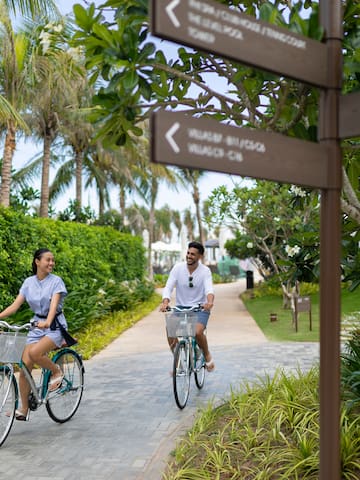 a man and woman riding bicycles on a path with trees and bushes