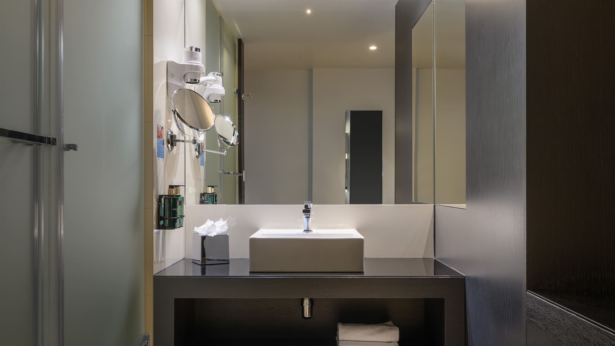 Modern hotel bathroom with vanity, rectangular sink, large mirror, and shower.