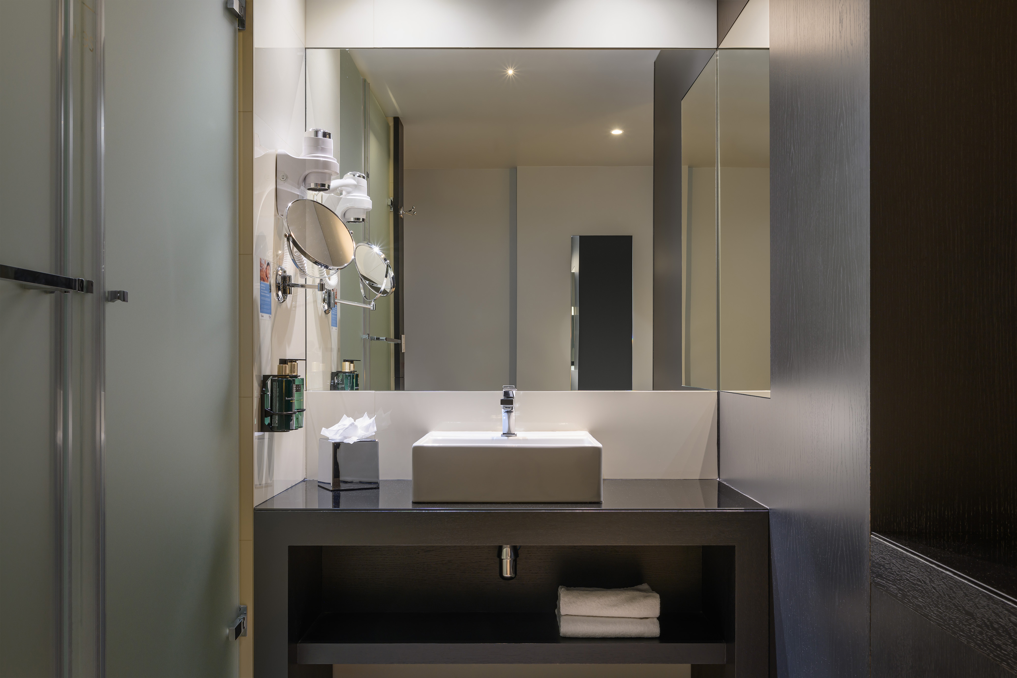 Modern hotel bathroom with vanity, rectangular sink, large mirror, and shower.