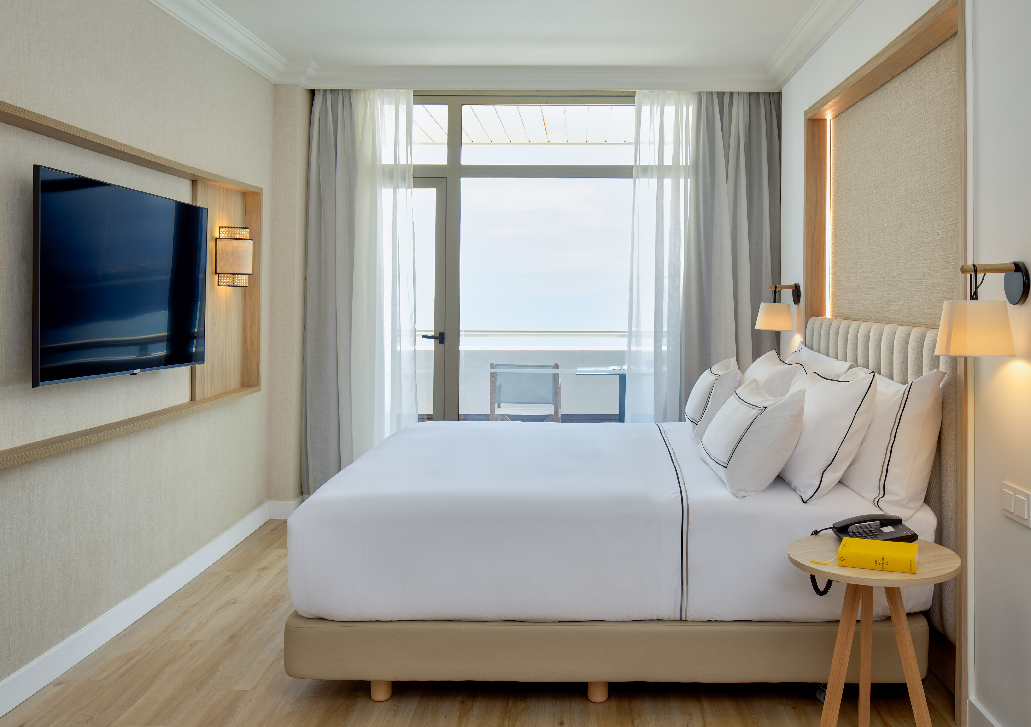 Modern hotel bedroom with bed, TV, and balcony ocean view.