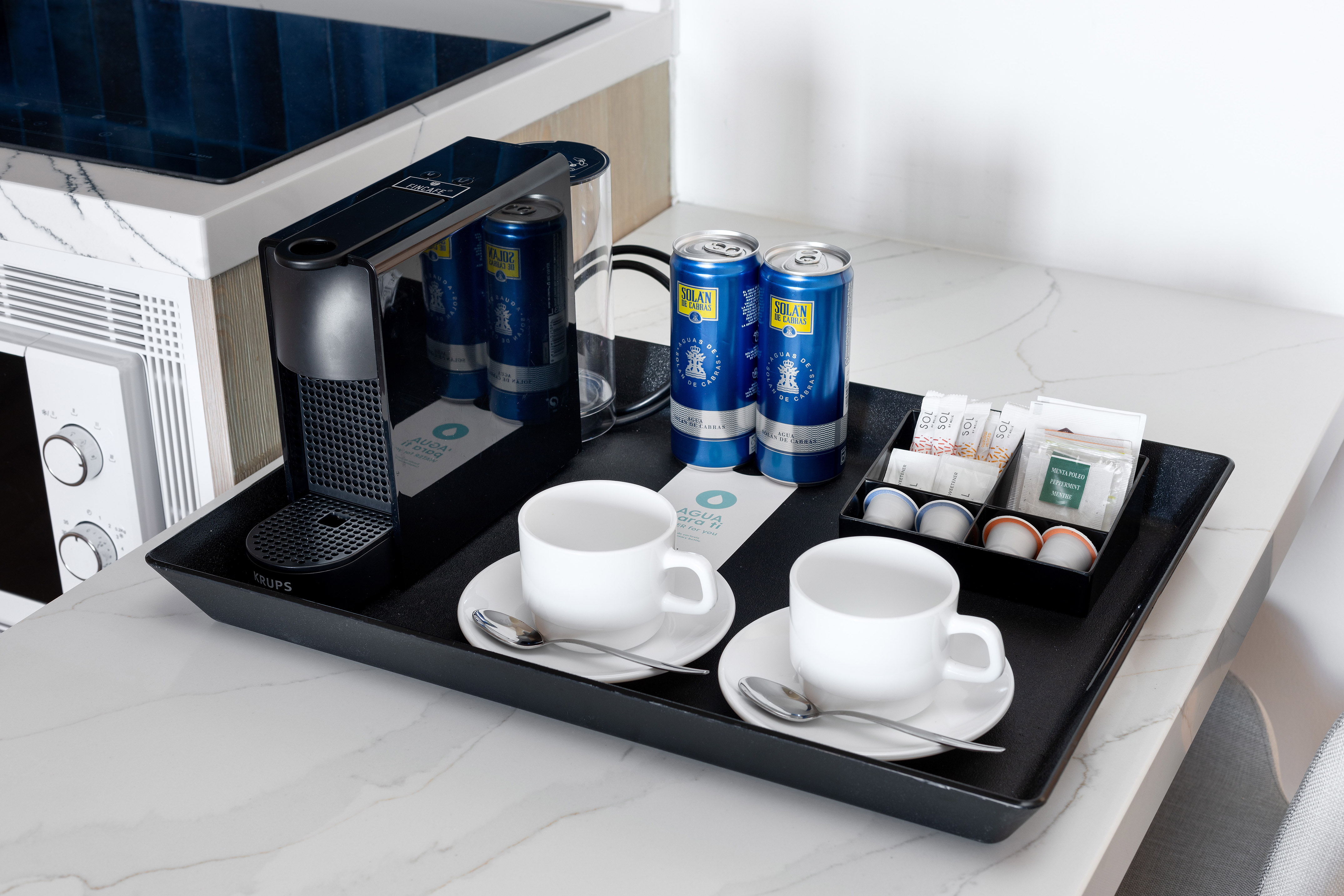 Hotel coffee station: Krups machine, cups, Solán de Cabras water, and coffee/tea pods.