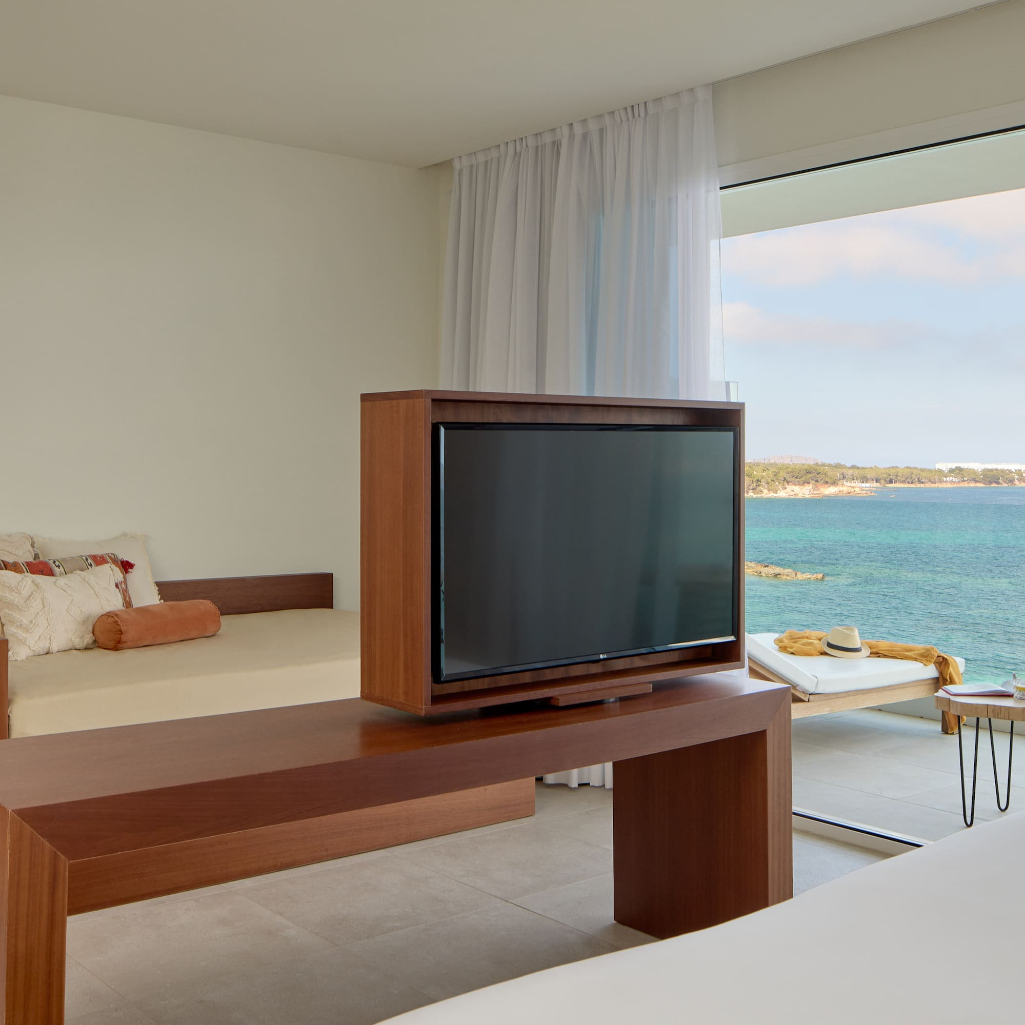 Ocean view hotel room with TV, daybed, and balcony overlooking blue sea.