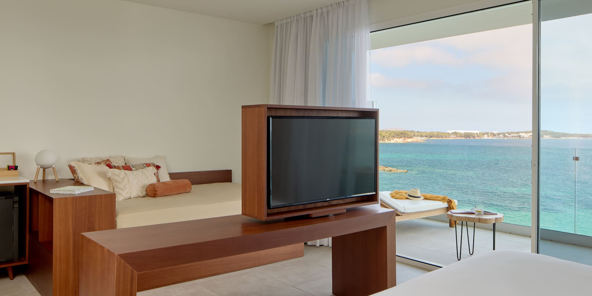 Ocean view hotel room with TV, daybed, and balcony overlooking blue sea.