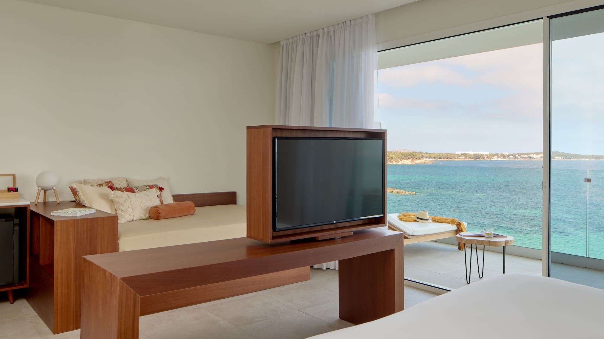 Ocean view hotel room with TV, daybed, and balcony overlooking blue sea.