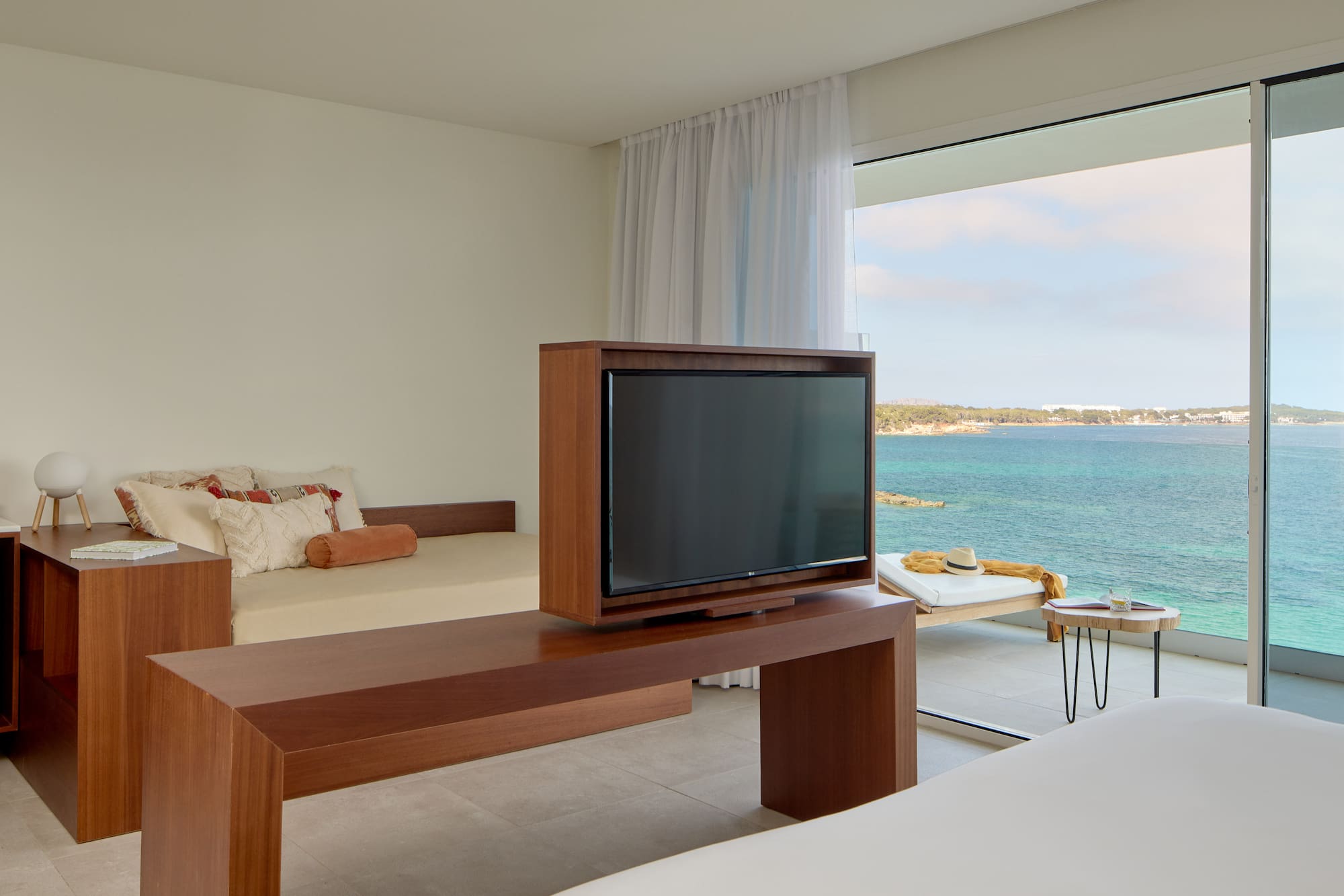 Ocean view hotel room with TV, daybed, and balcony overlooking blue sea.